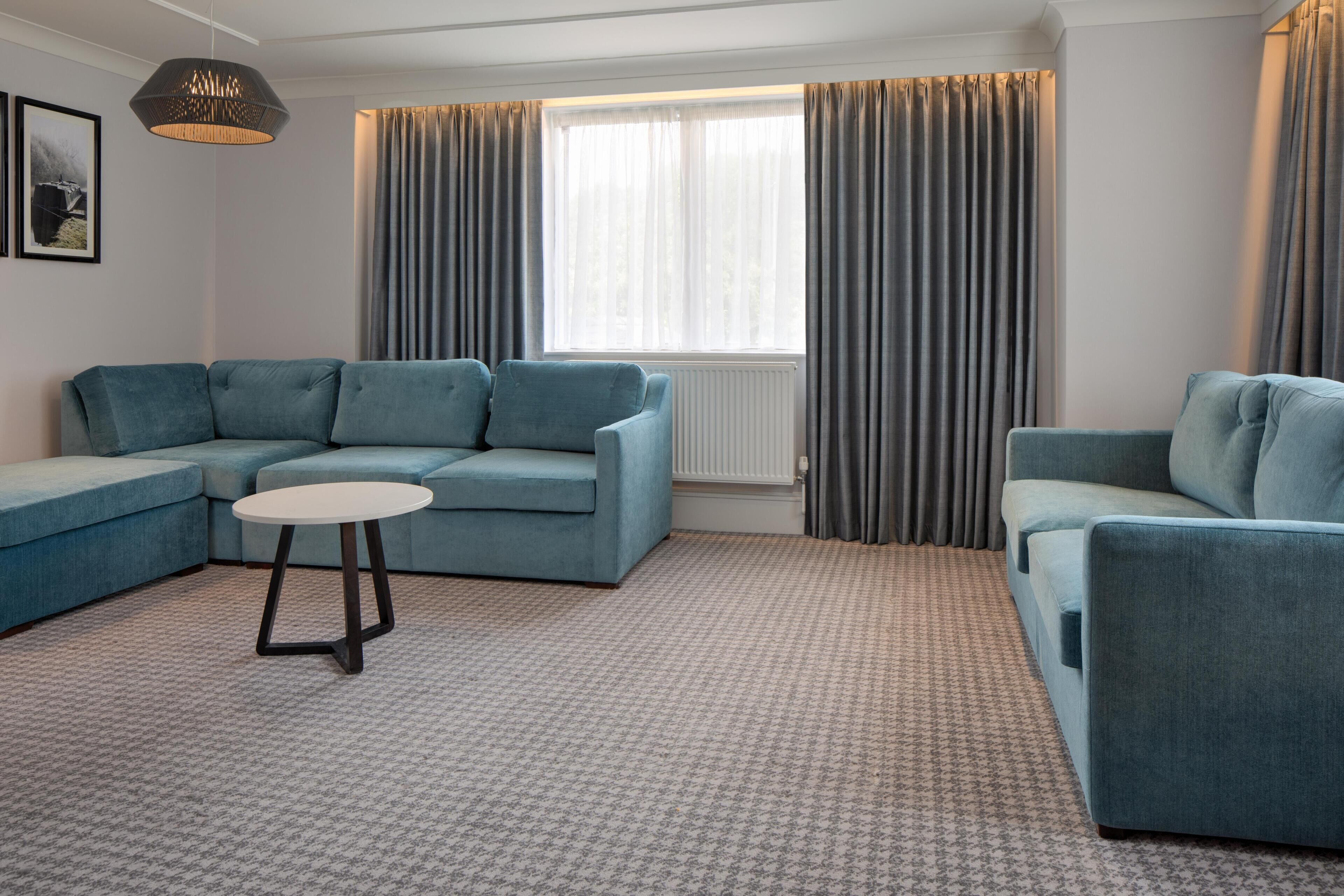 A modern living room with a sectional sofa, a round coffee table, and a large window with curtains.