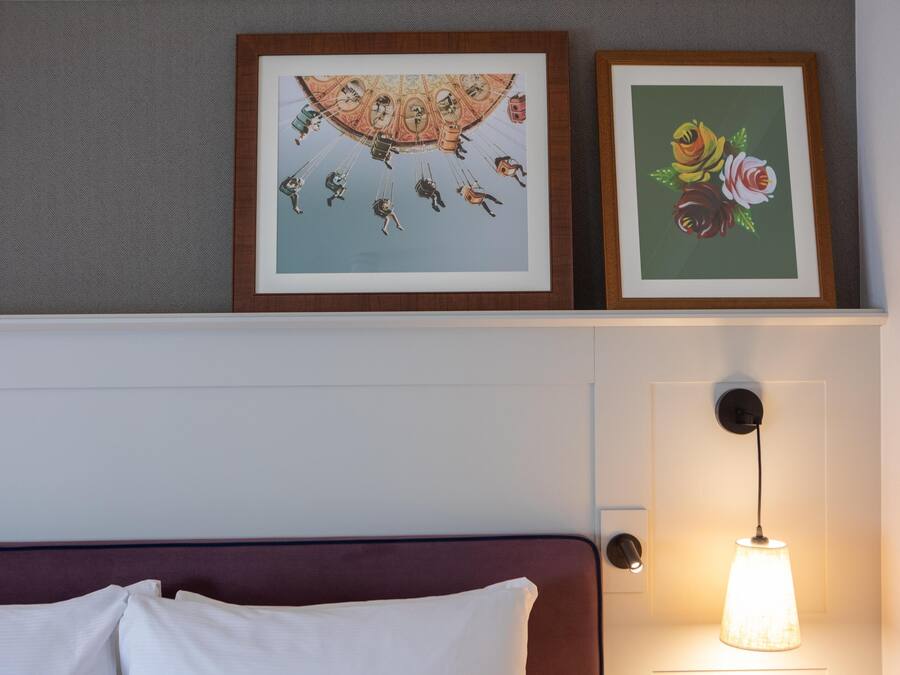 Un lit avec des oreillers blancs, une tête de lit et une lampe fixée au mur.