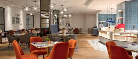 A modern hotel lobby with multiple seating areas, a central dining table, and a kitchen counter.