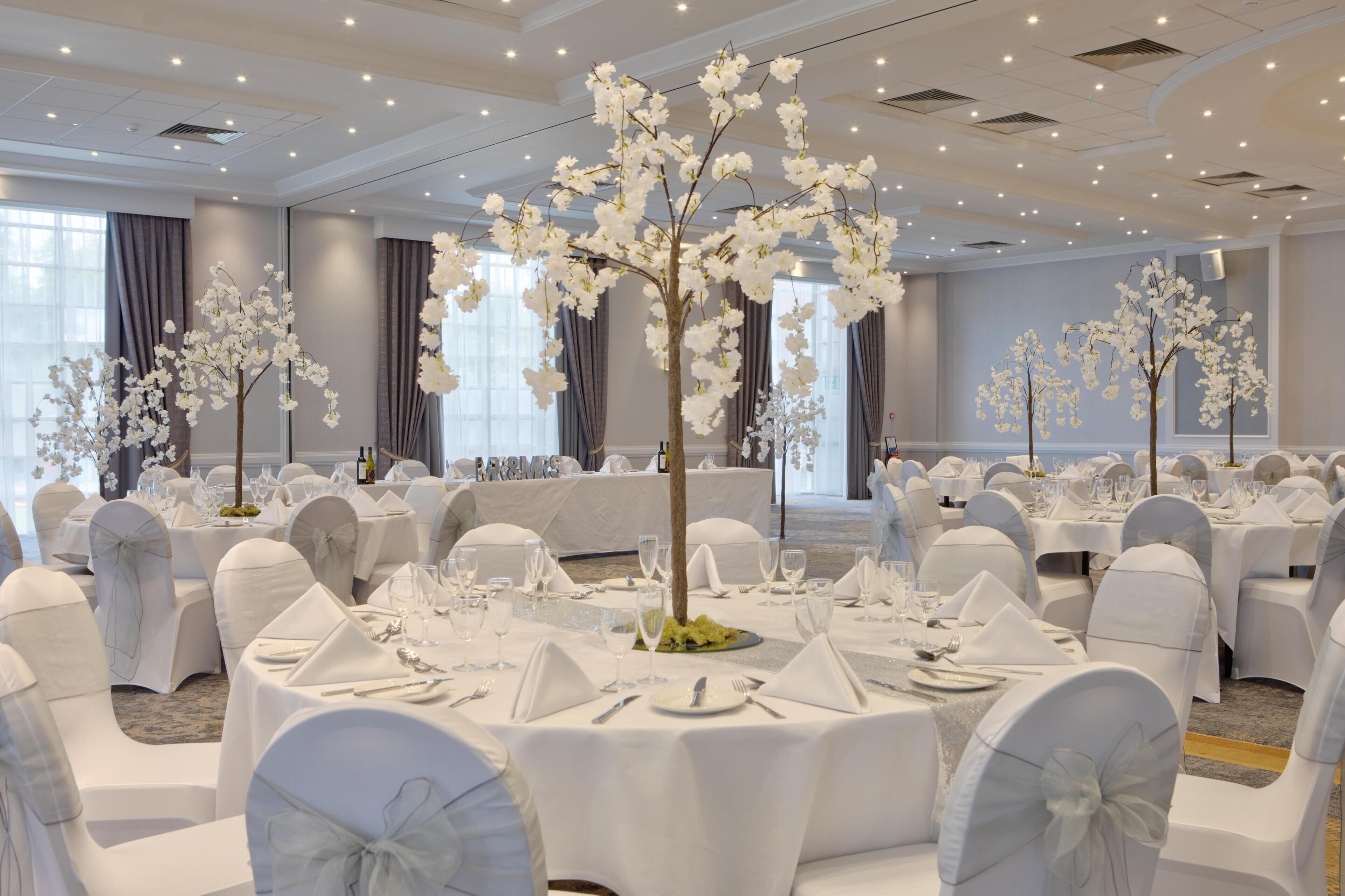 A banquet hall with round tables, white chairs, and floral centerpieces.