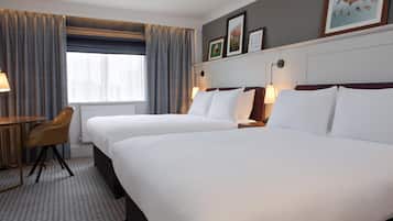 A hotel room with two beds, a desk, a chair, a window with curtains, and wall-mounted artwork.