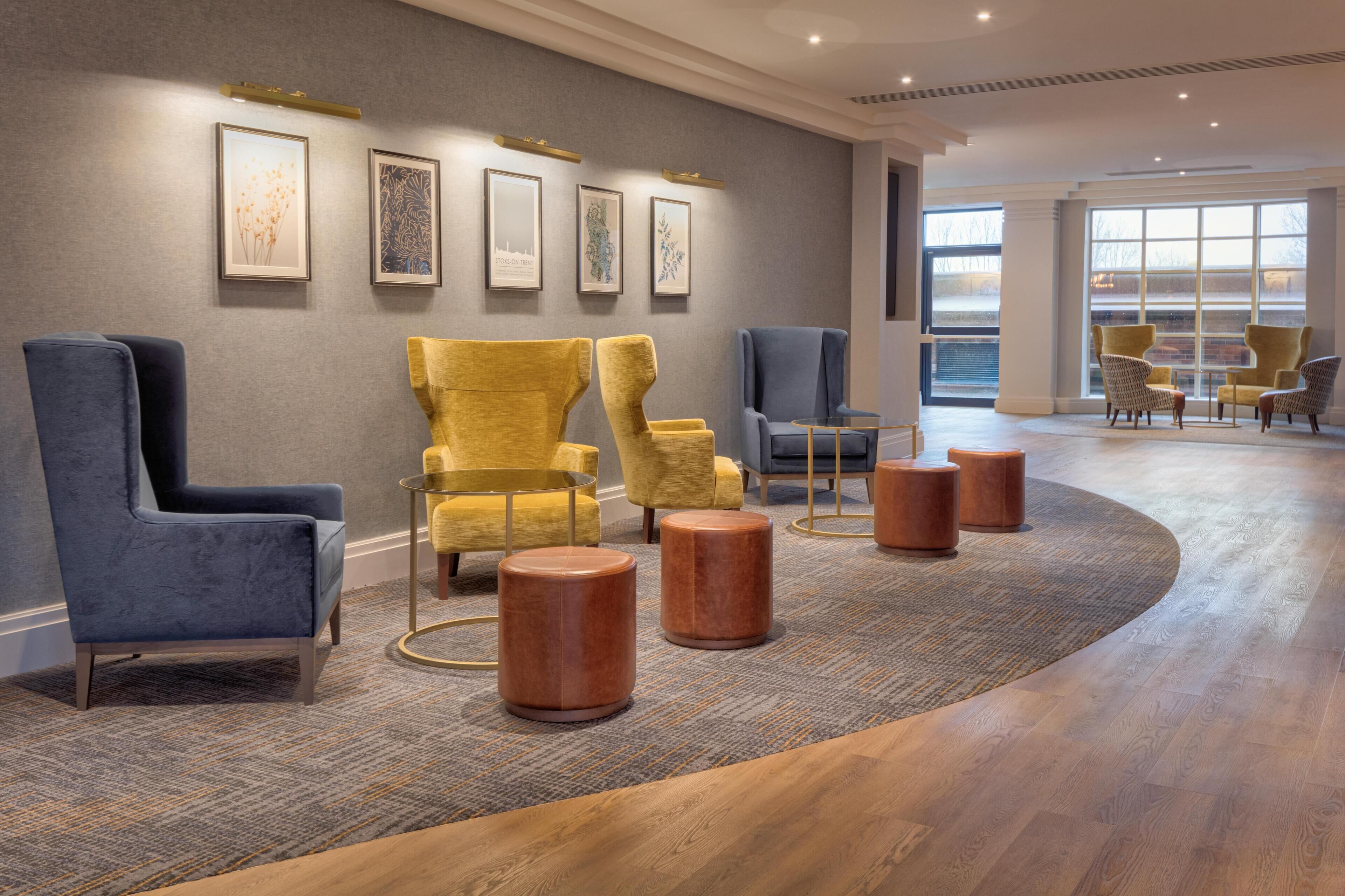 A modern lobby with a curved carpet, a seating area with blue and yellow chairs, and framed artwork on the wall.