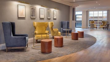 A modern lobby with a curved carpet, a seating area with blue and yellow chairs, and framed artwork on the wall.