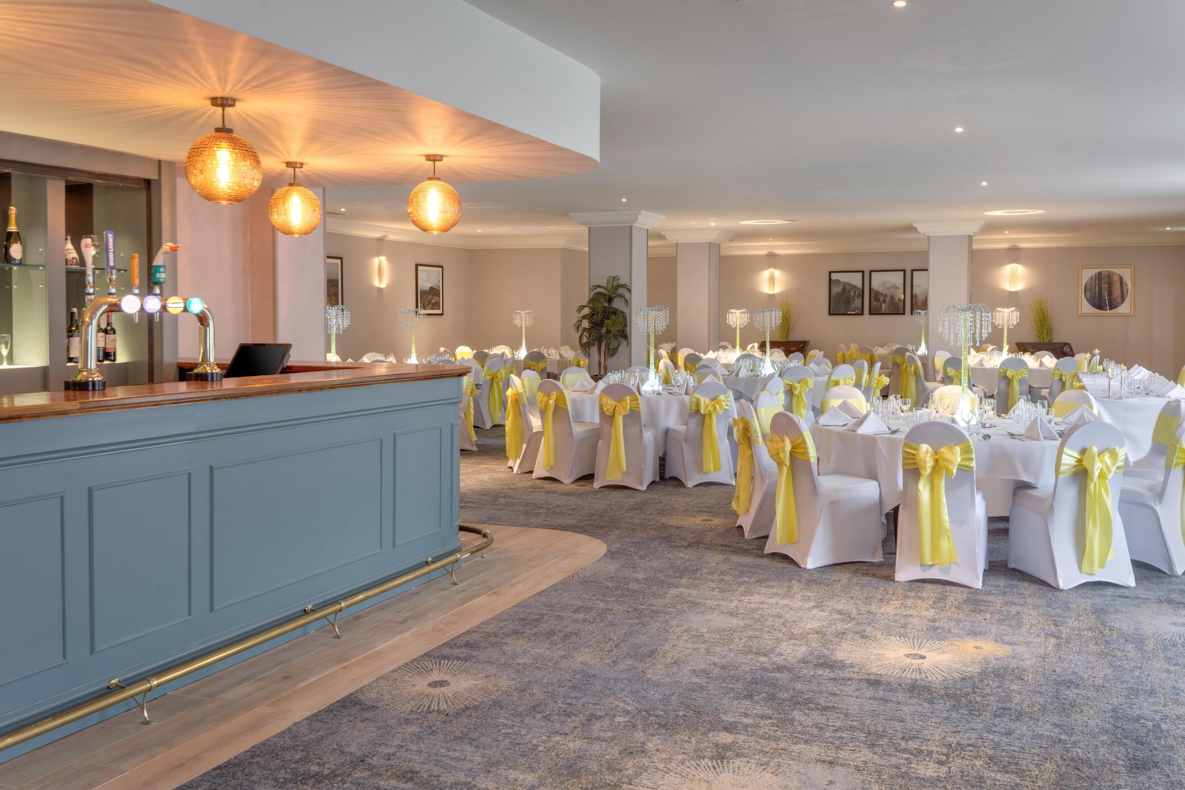A banquet hall with round tables, white tablecloths, and yellow sashes.