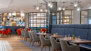 A modern dining area with booths, tables, and chairs, featuring a mix of wood and fabric materials. - DoubleTree by Hilton Stoke on Trent (Stoke-on-Trent)