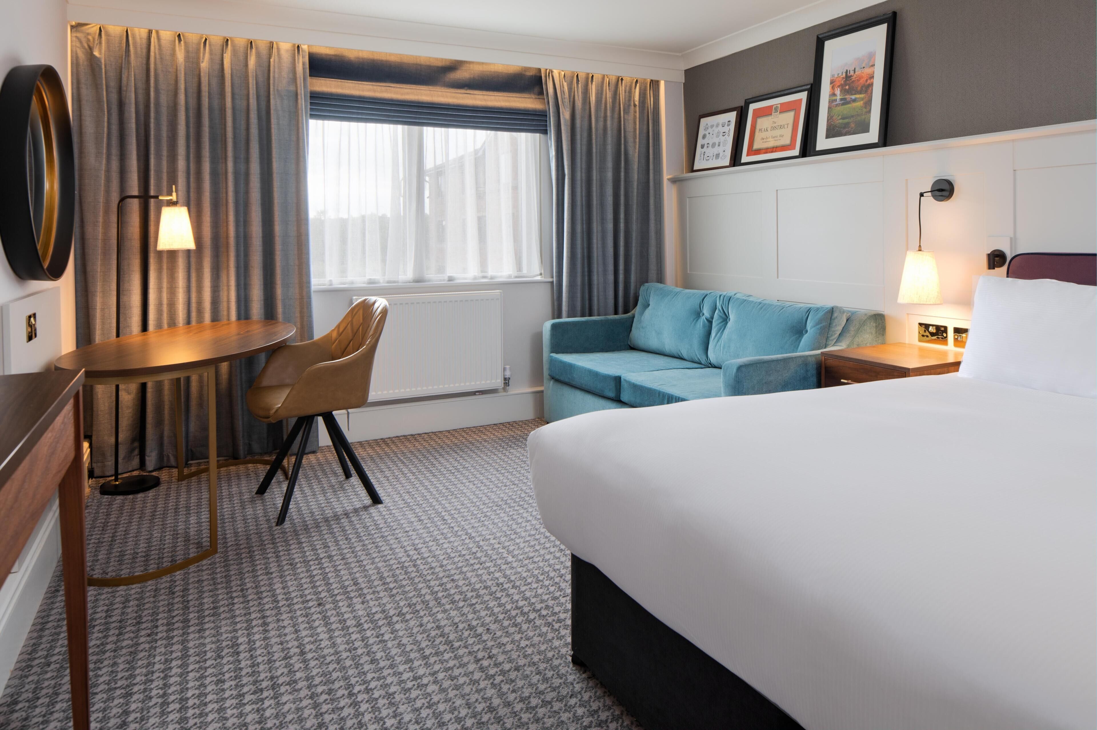 A hotel room with a bed, a sofa, a chair, a small table, and a window with curtains.