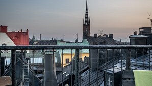 A rooftop terrace with a table set for two, featuring a bottle of champagne, glasses, and a bowl of fruit. The terrace overlooks a cityscape with buildings and a church spire. - Lord Nelson Hotel (Stockholm)