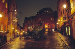 A cobblestone street lined with historic buildings, illuminated by street lamps and featuring a prominent sign for a hotel. - Lord Nelson Hotel (Stockholm)