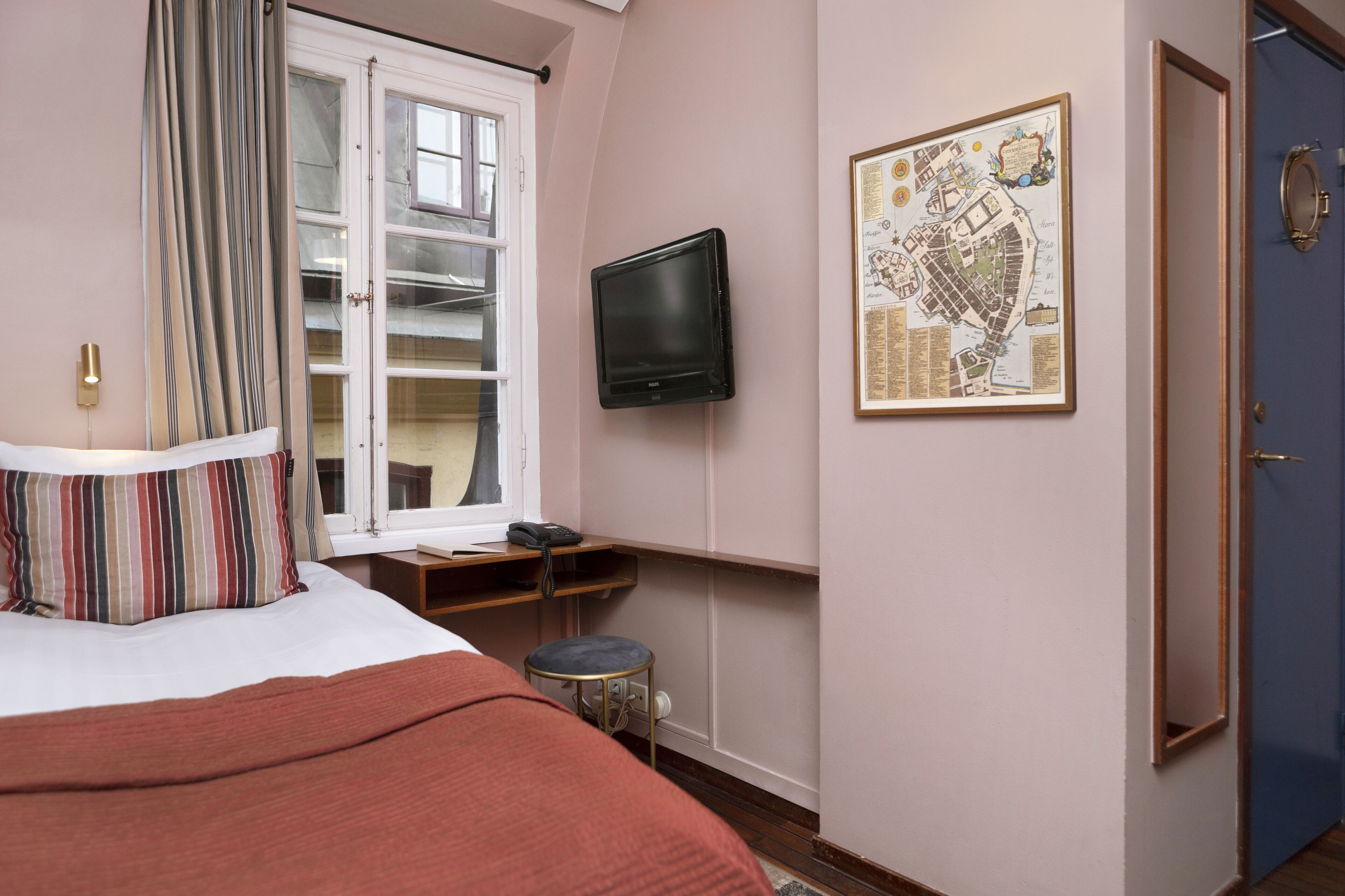 A bedroom with a bed, a television mounted on the wall, a window with curtains, and a map on the wall.