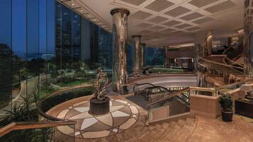 A modern hotel lobby with a central column, a spiral staircase, and a view of the cityscape through large windows.
