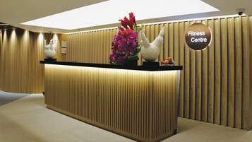 Un mostrador de recepción con un letrero que dice "Fitness Centre" en un interior moderno con paneles de madera verticales y una luz empotrada en el techo.