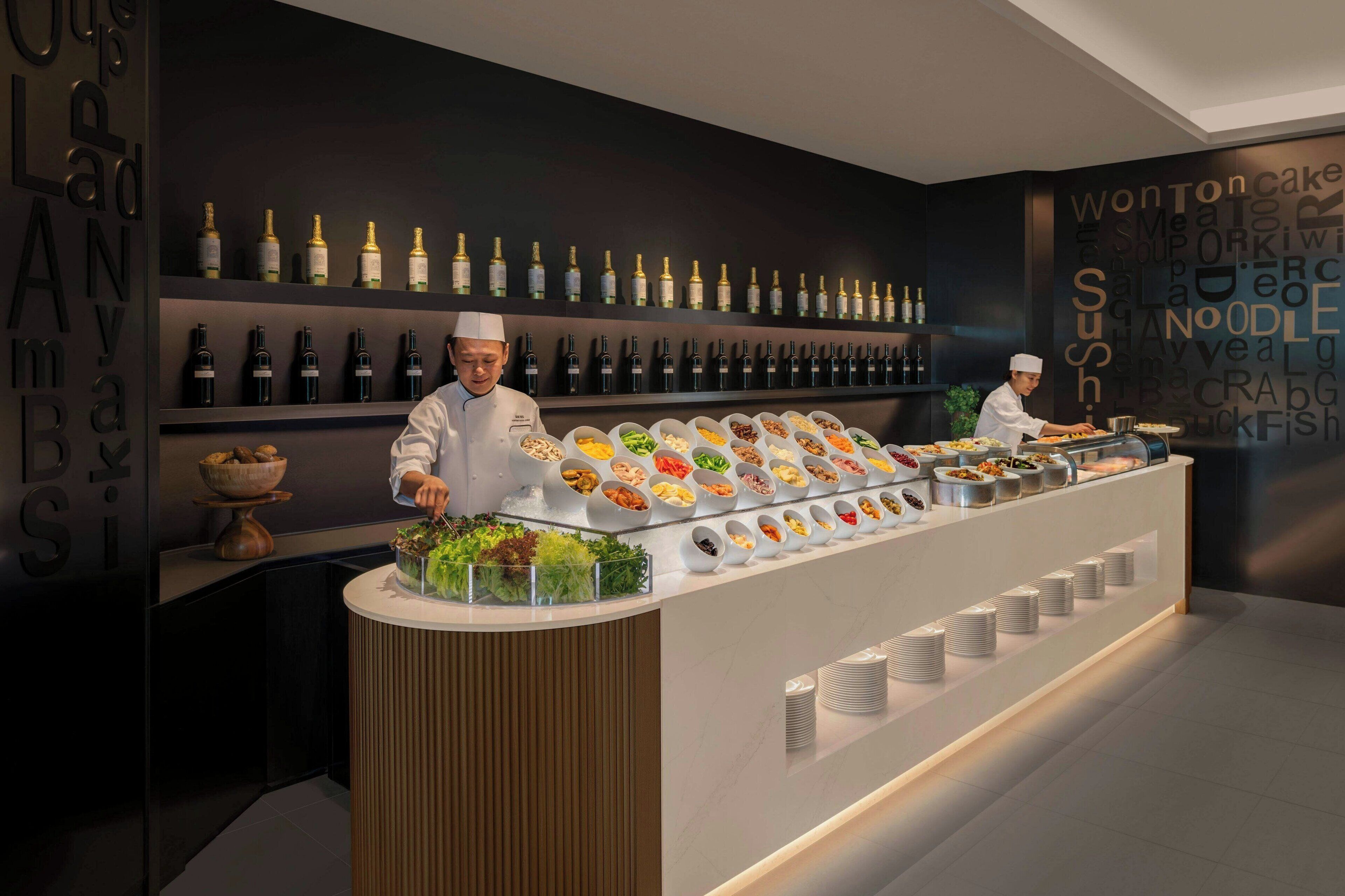 Disposição de buffet com diversos alimentos e uma seleção de garrafas de vinho.