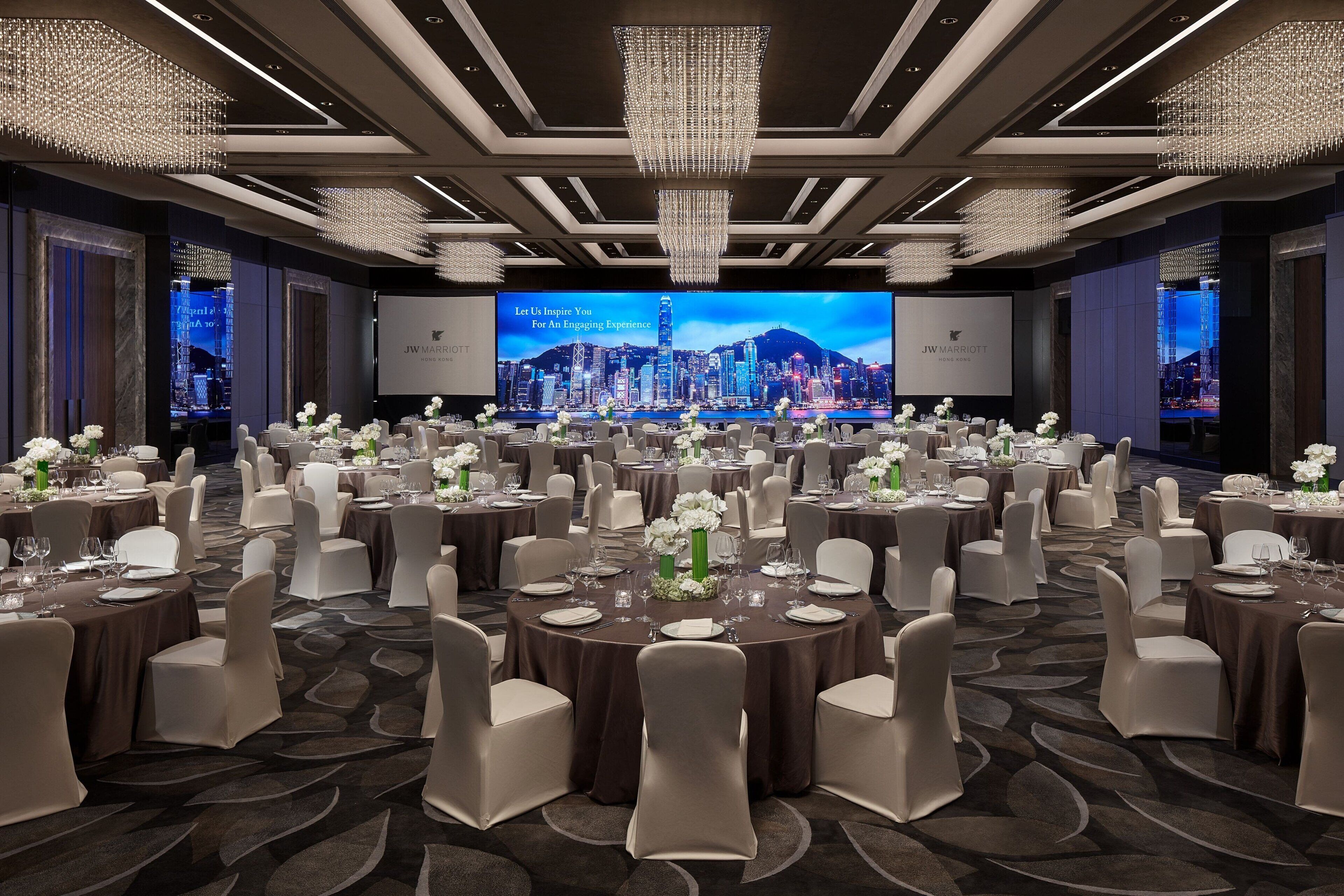 A spacious conference room with round tables, white chairs, and a large screen displaying a cityscape.