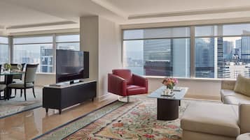 A modern living room with a flat-screen TV, a red armchair, a beige sofa, and a large window offering a city view.