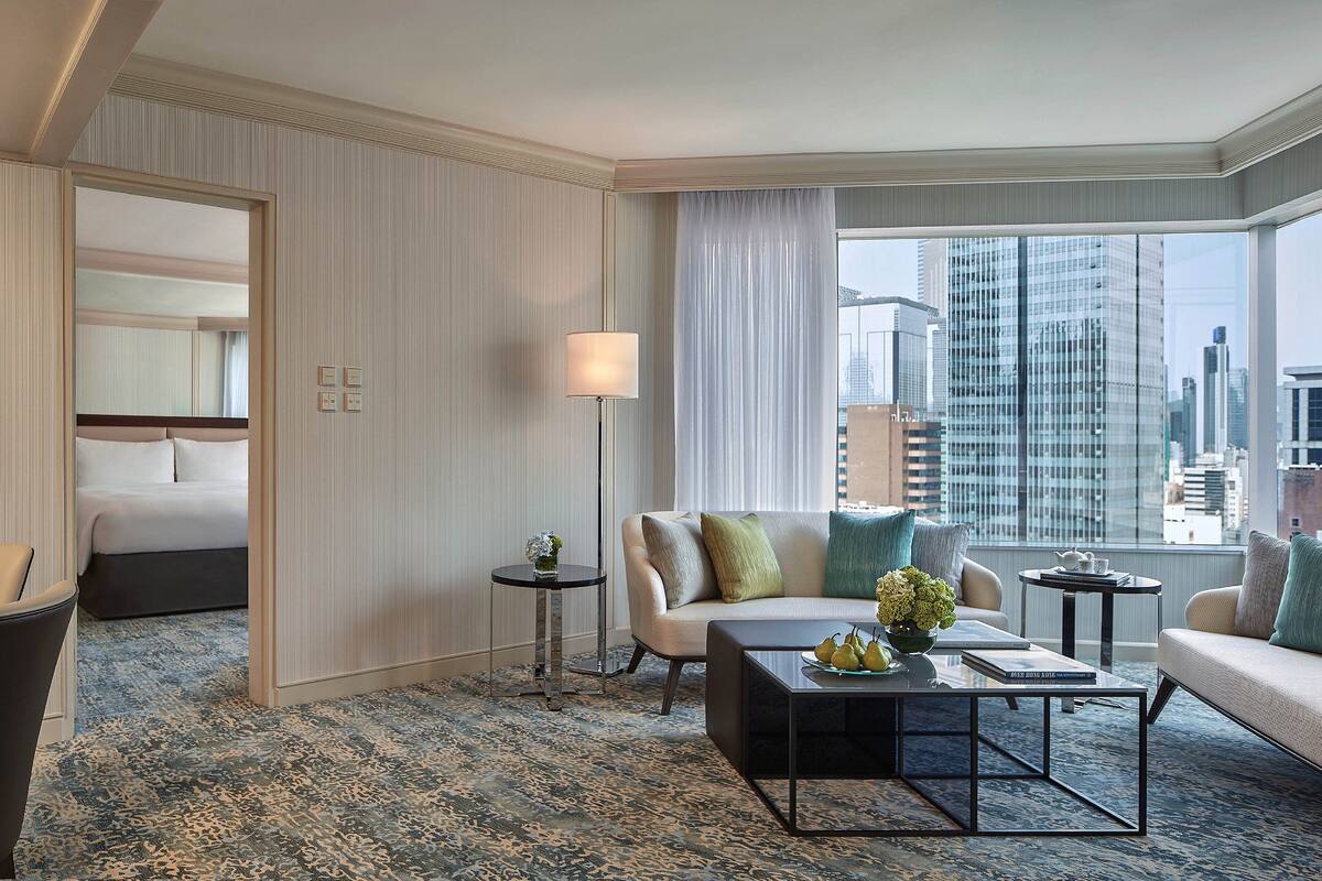 A hotel room with a bed, a sofa, a coffee table, and a view of the cityscape.