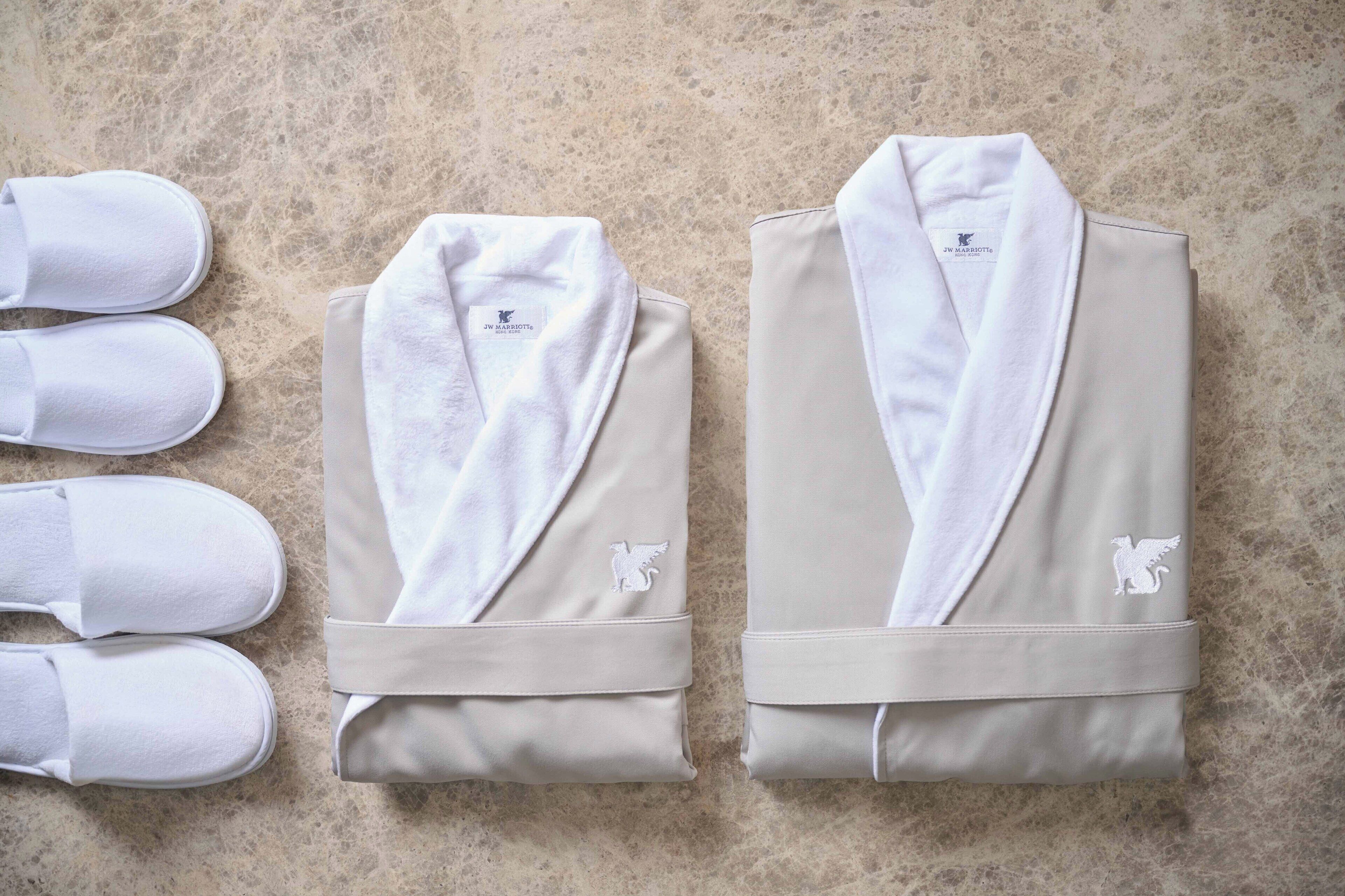 A pair of white bathrobes and slippers on a textured floor.