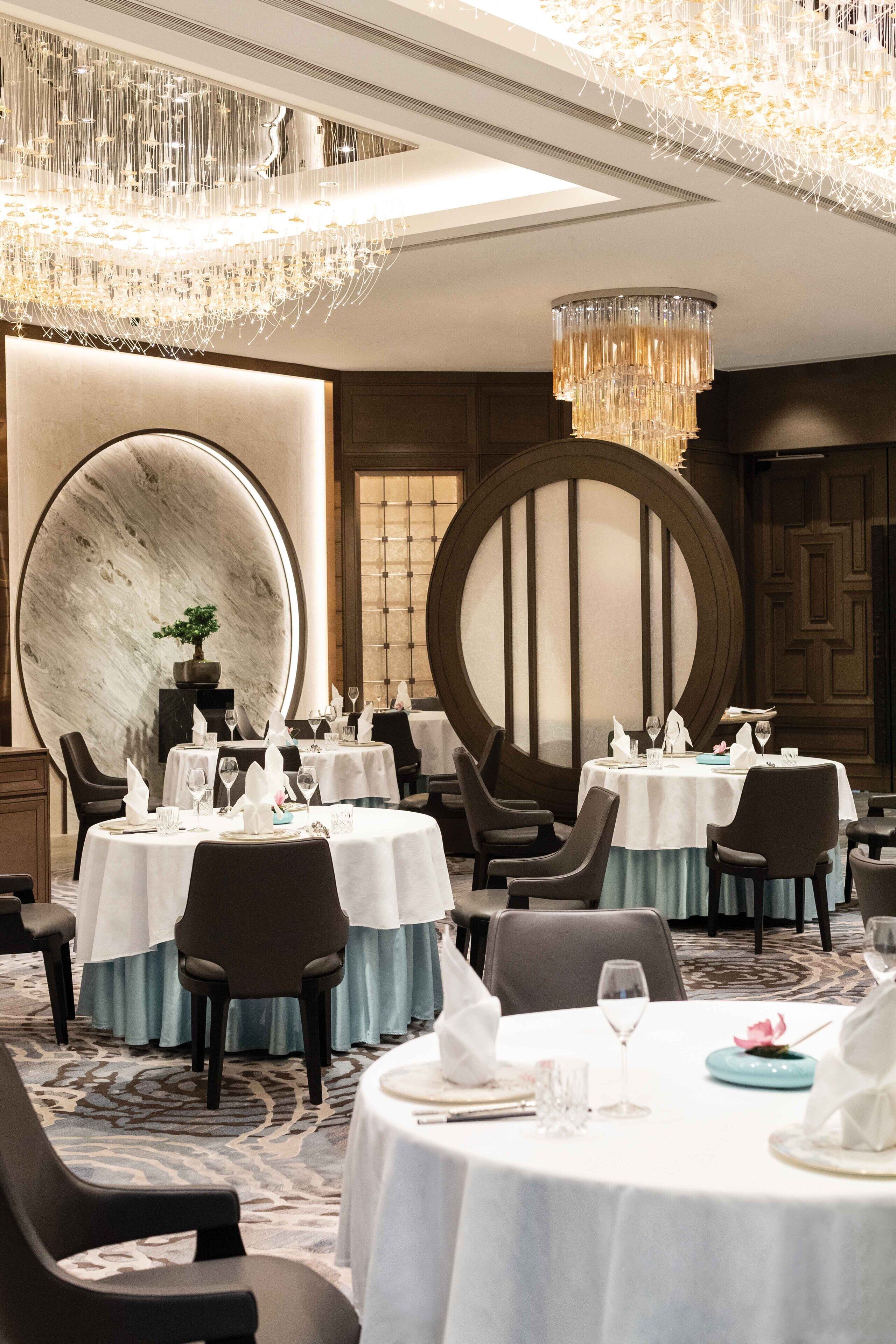 A dining area with round tables, chairs, and a chandelier.