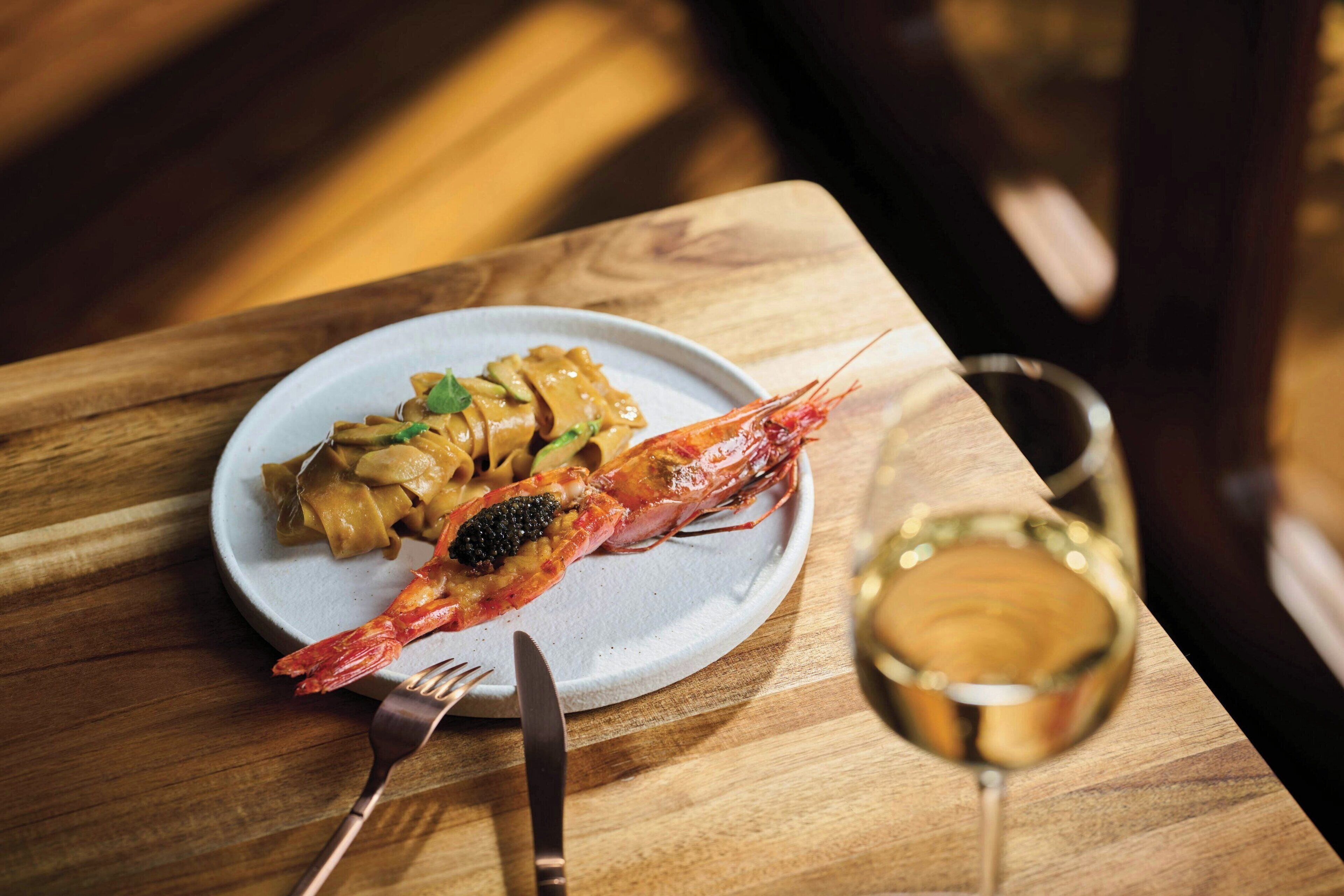 Une assiette de pâtes et une crevette cuite sur une table en bois.