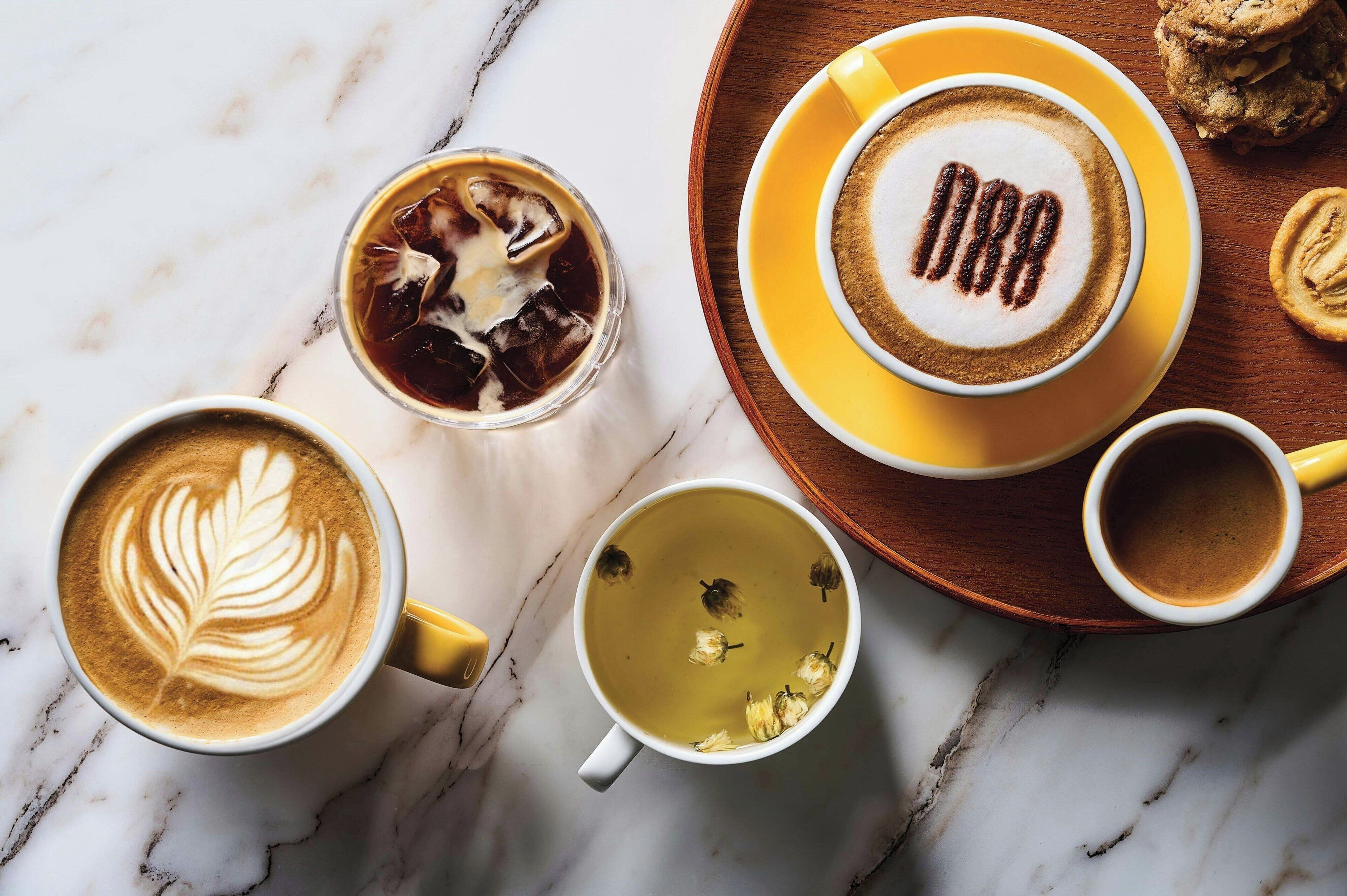 A variety of coffee drinks on a marble surface, including a latte with a leaf design, a cup with a heart design, and a cup with a heart and leaf design.