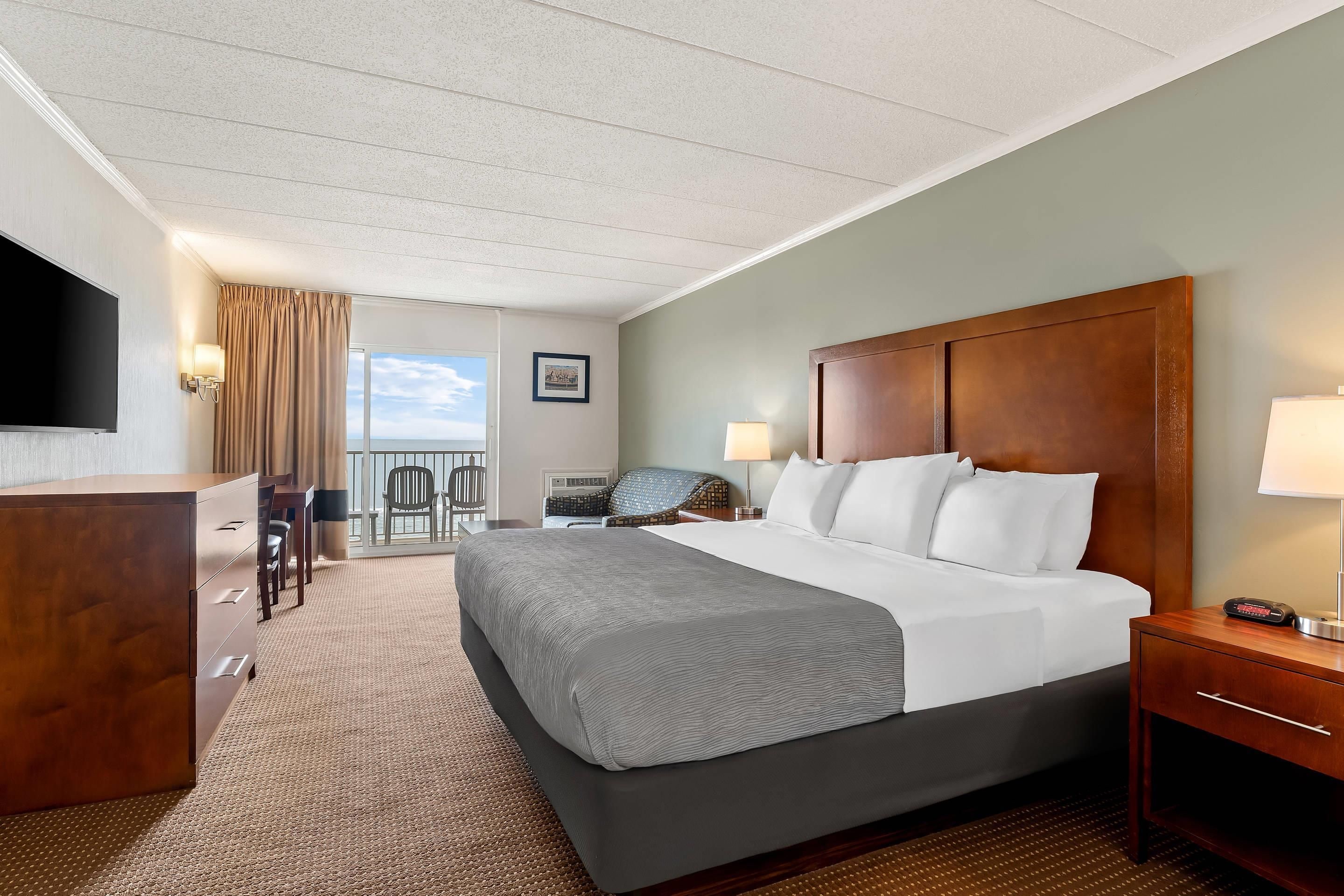 A hotel room with a large bed, a desk, a chair, a TV, and a view of the ocean.