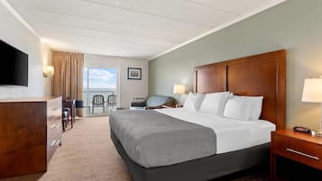 A hotel room with a large bed, a desk, a chair, a TV, and a view of the ocean.