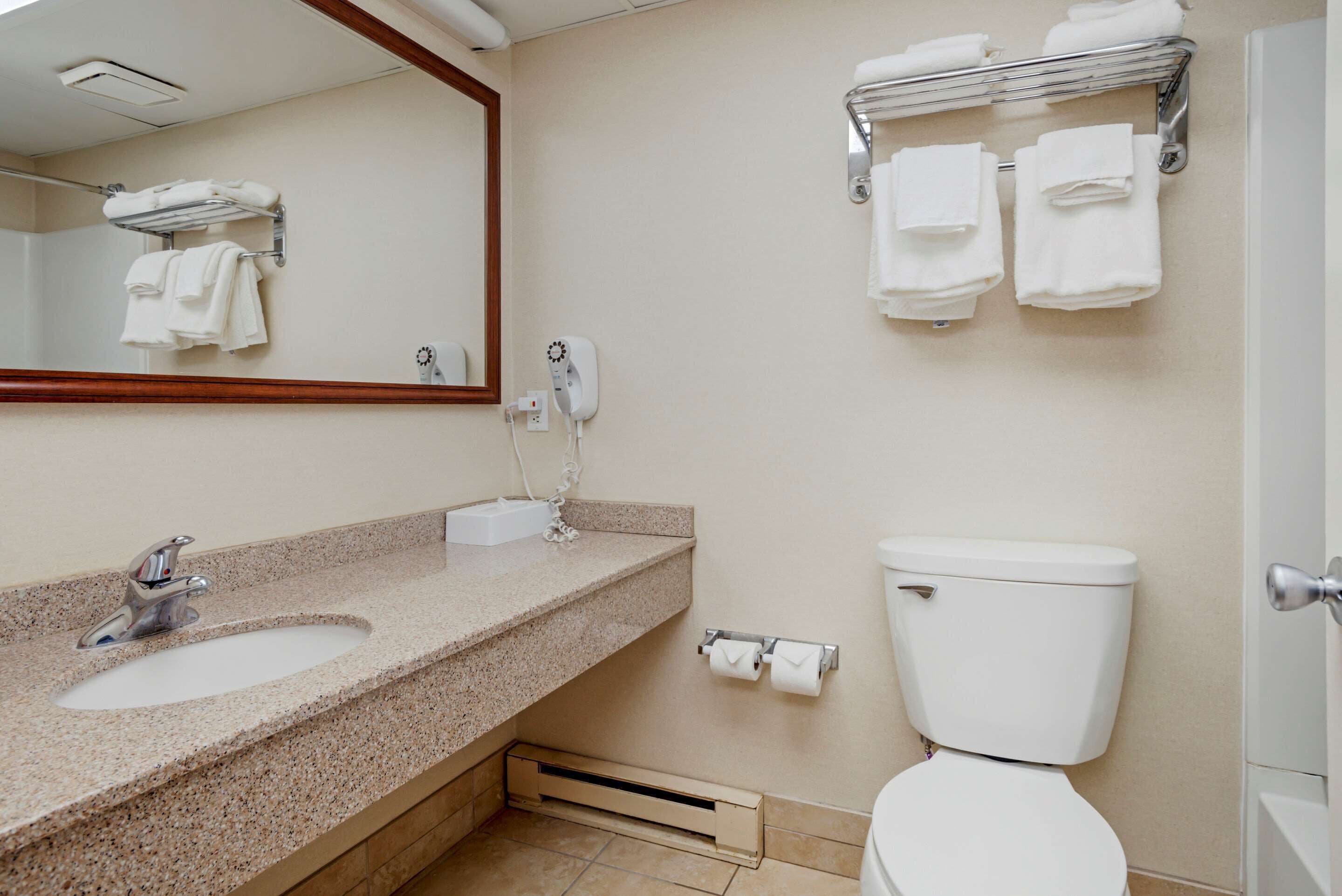 A bathroom with a sink, mirror, towel rack, toilet, and a towel dispenser.