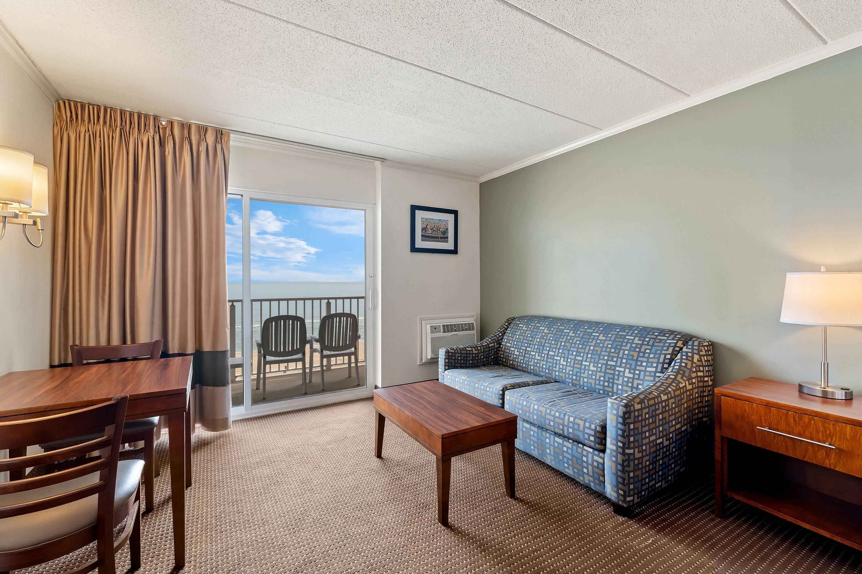 A hotel room with a balcony, a sofa, a dining table, and a lamp.