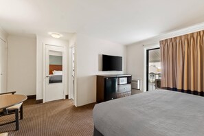 A hotel room with a bed, a desk, a television, a minibar, and a view of the outside. - Quality Inn Ocean City Beachfront (Ocean City)