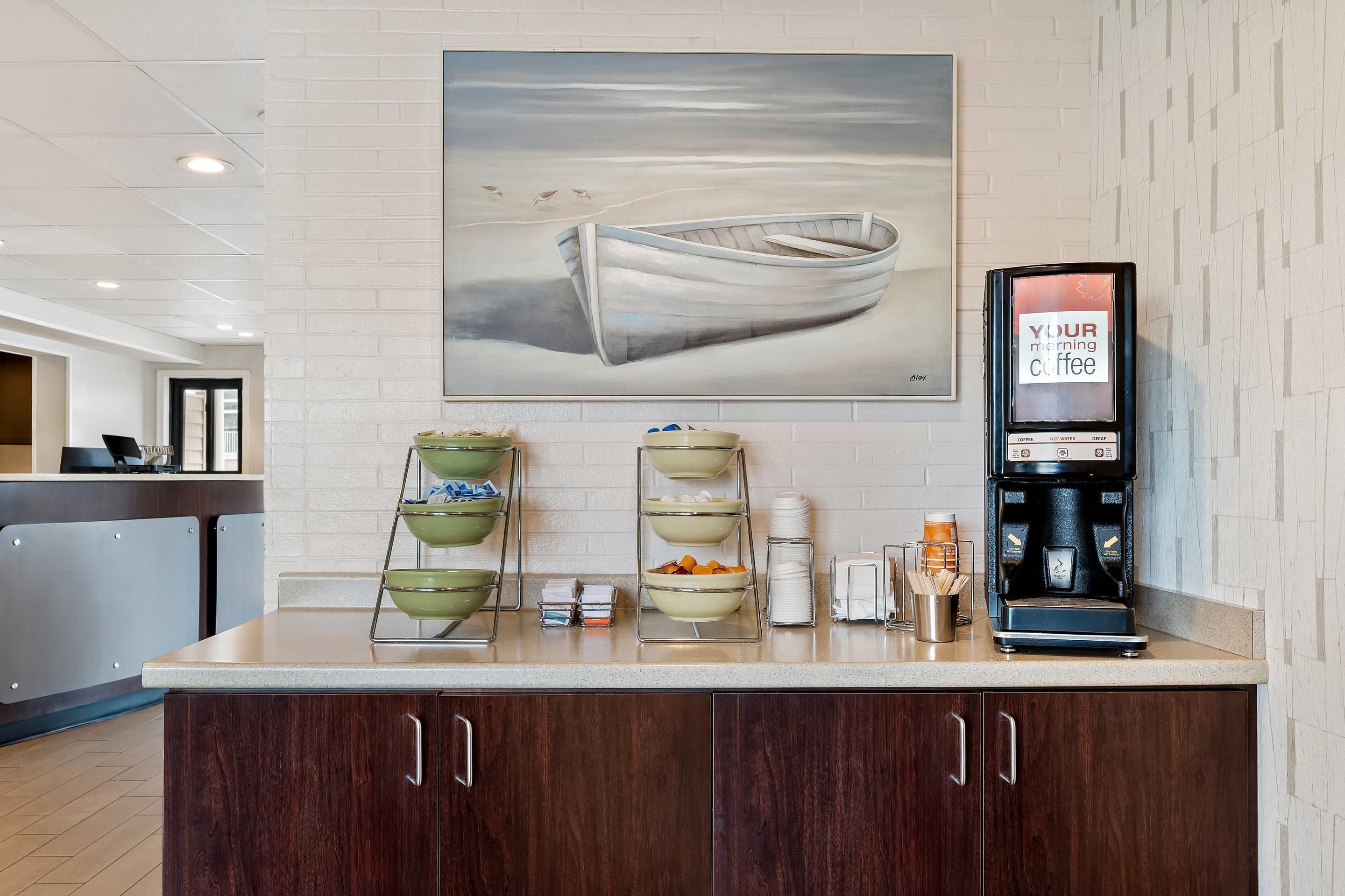 A counter with a coffee machine, bowls, and a painting of a boat on the wall.
