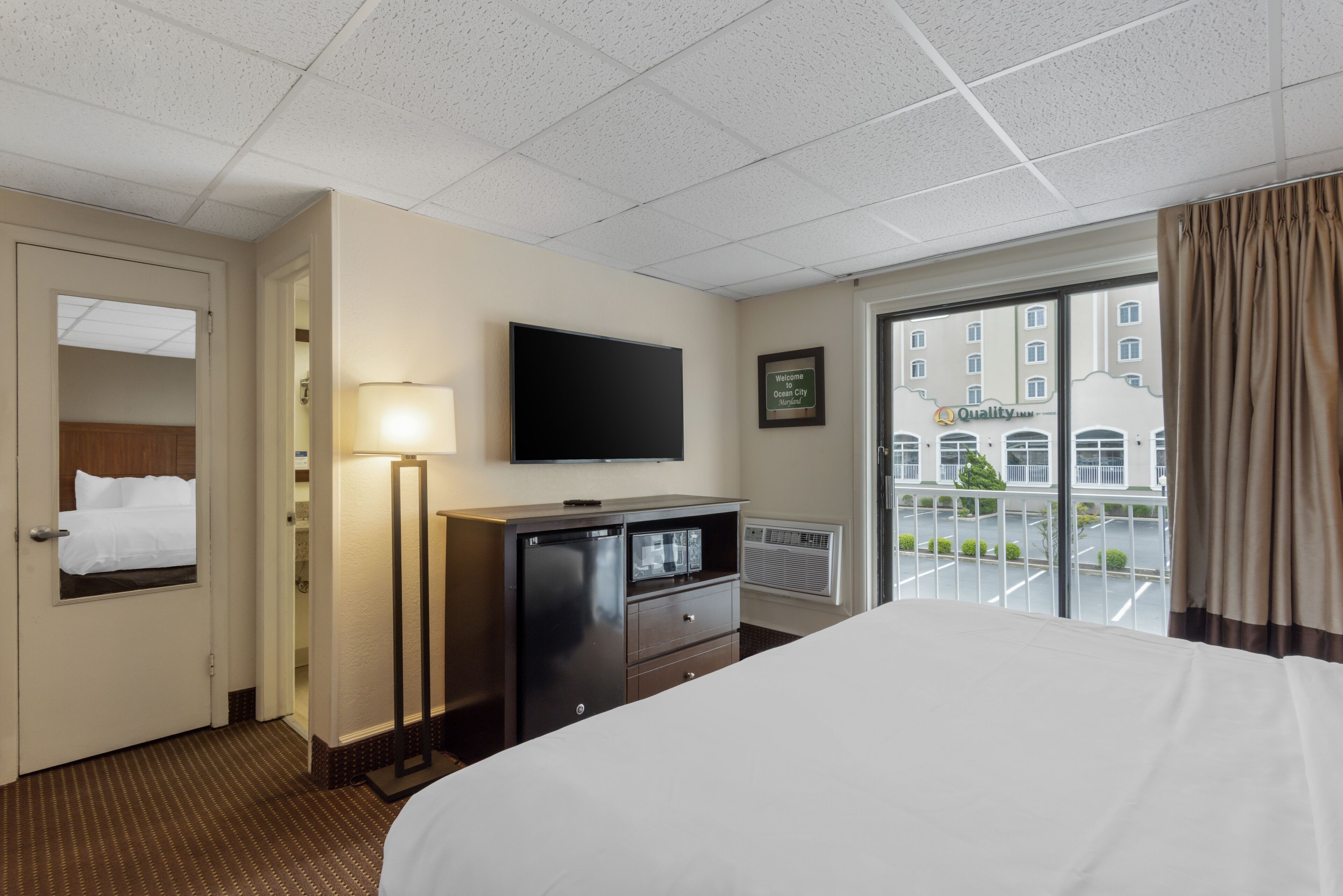 A hotel room with a bed, a desk with a flat-screen TV, a lamp, and a window with a view of the city.