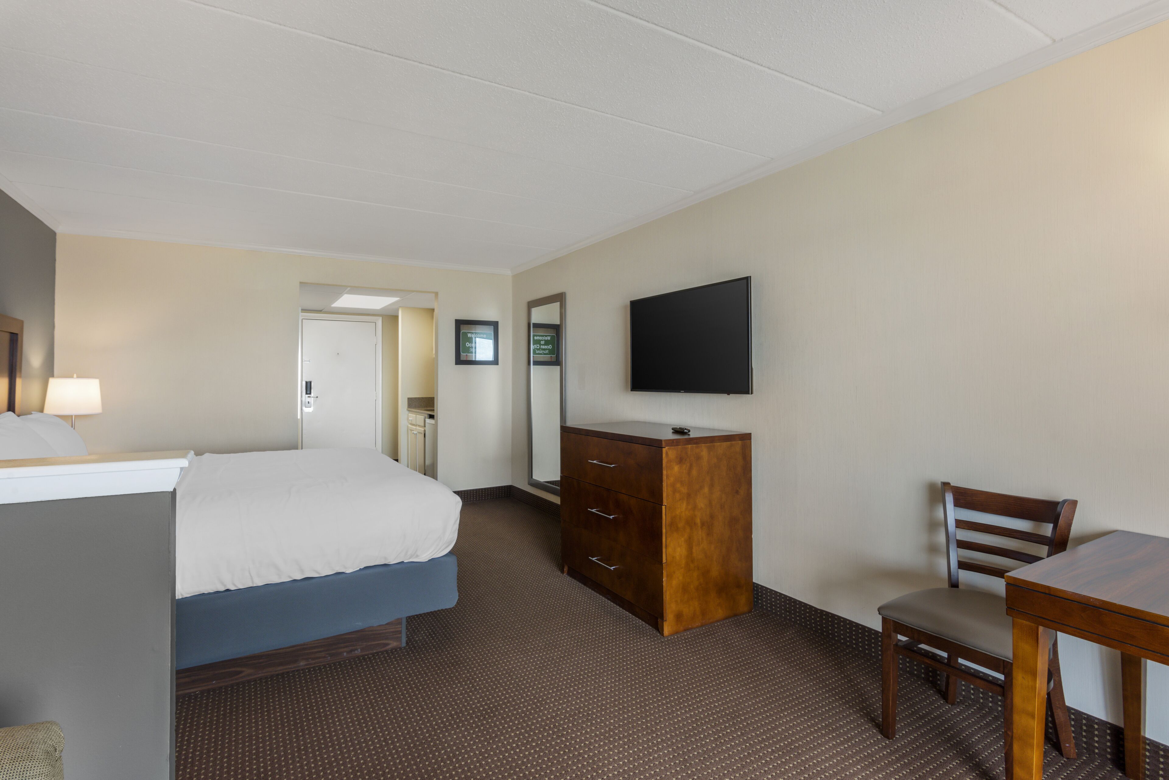 A hotel room with a bed, a dresser, a television, and a desk with a chair.