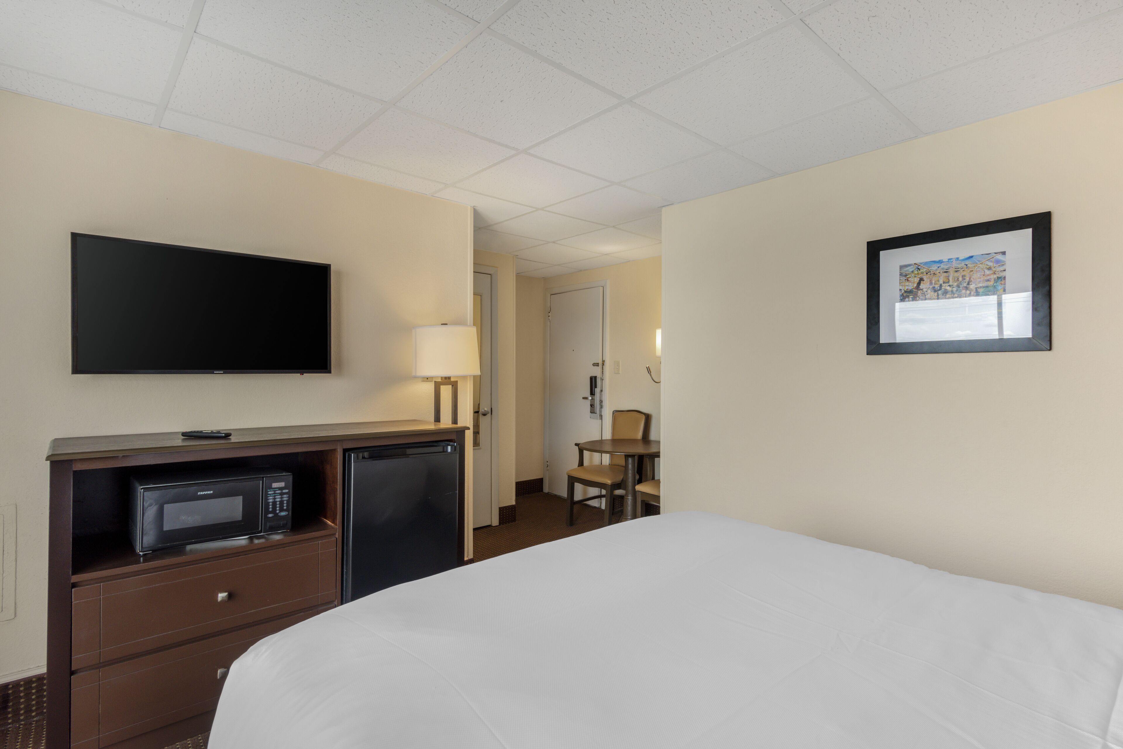 A hotel room with a bed, a television, a microwave, a refrigerator, a desk, and a chair.