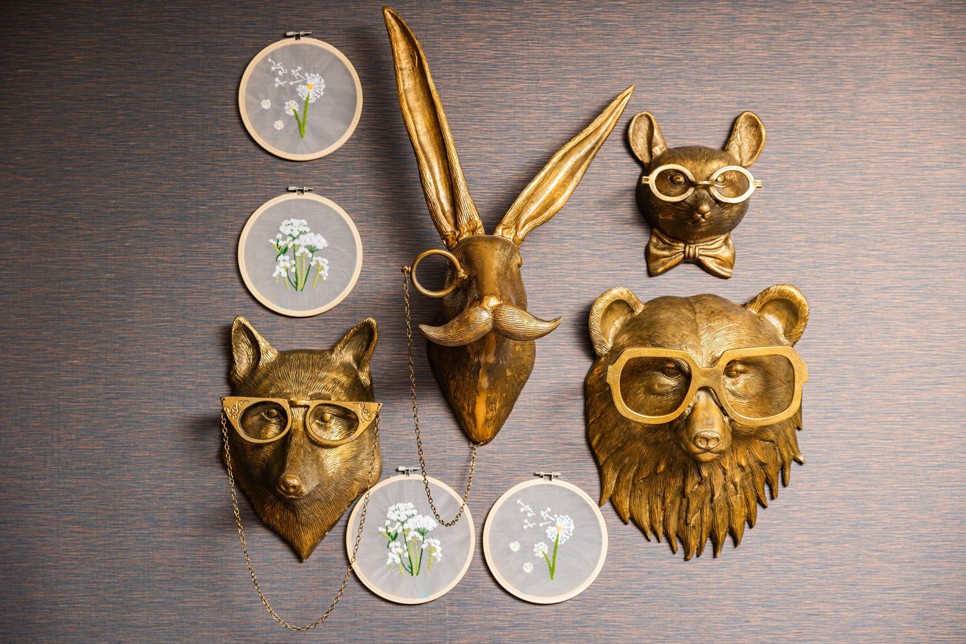 Une collection d’objets décoratifs comprenant des têtes d’animaux et des motifs floraux brodés, le tout disposé sur une surface en bois.