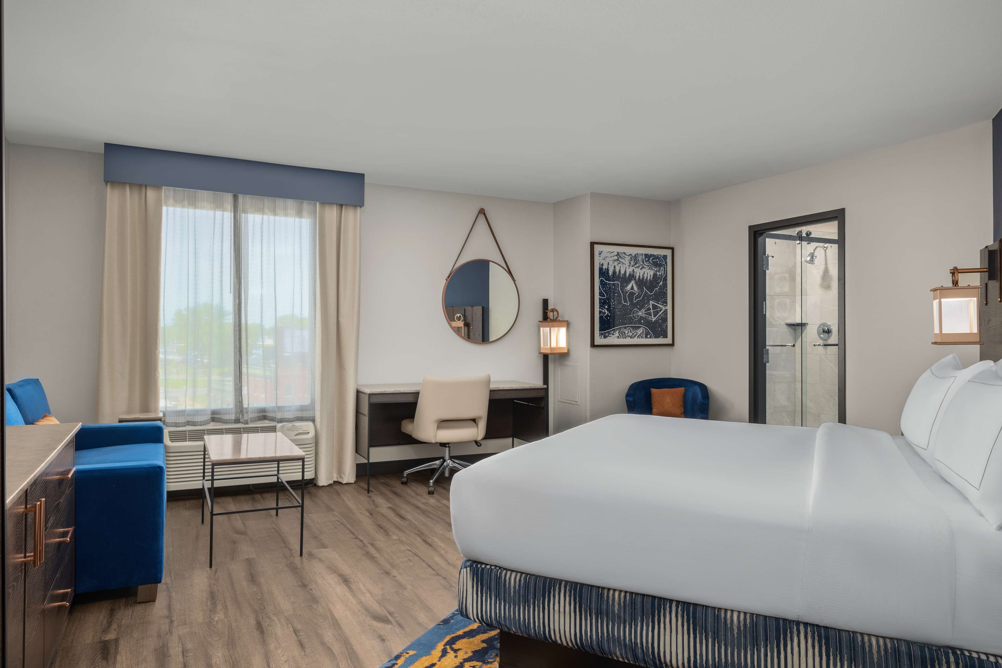 A hotel room with a large bed, a desk with a chair, a small table, and a sofa.
