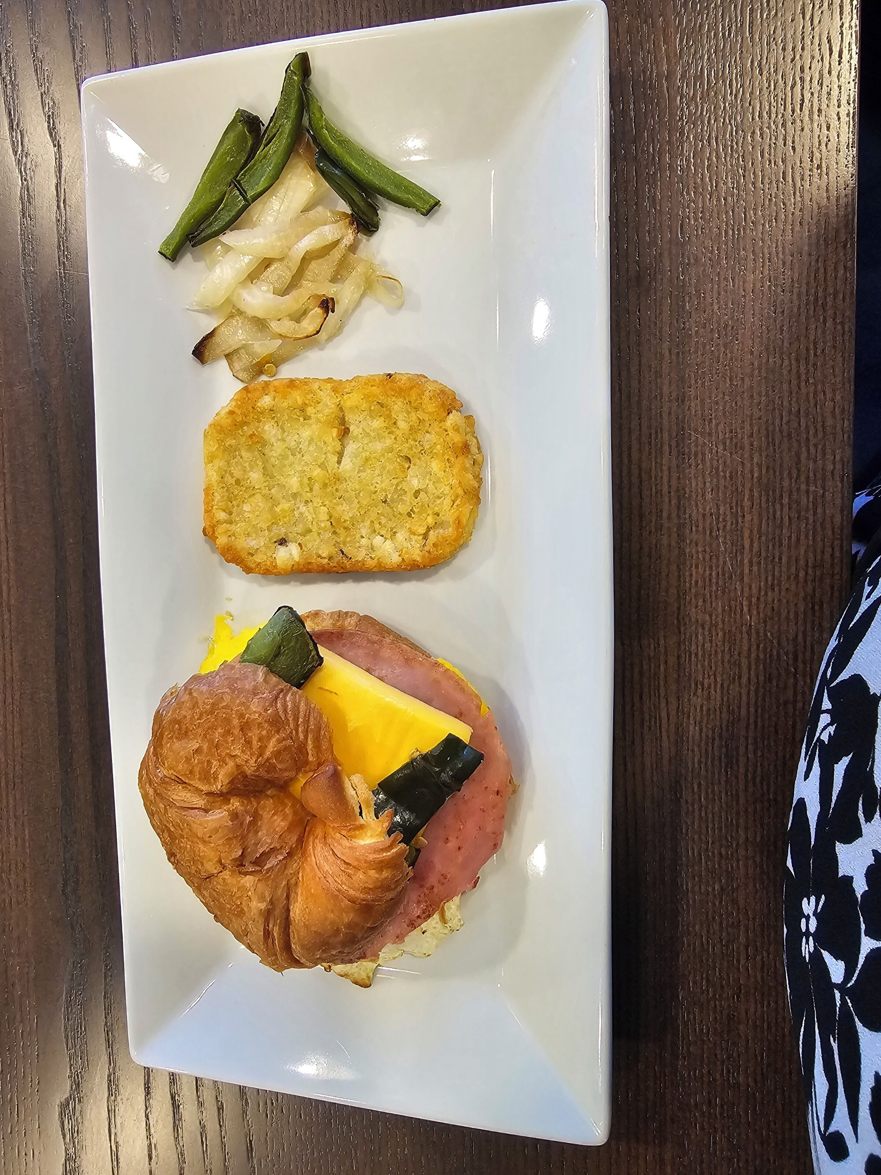 Un plato con un croissant, jamón, queso y verduras.