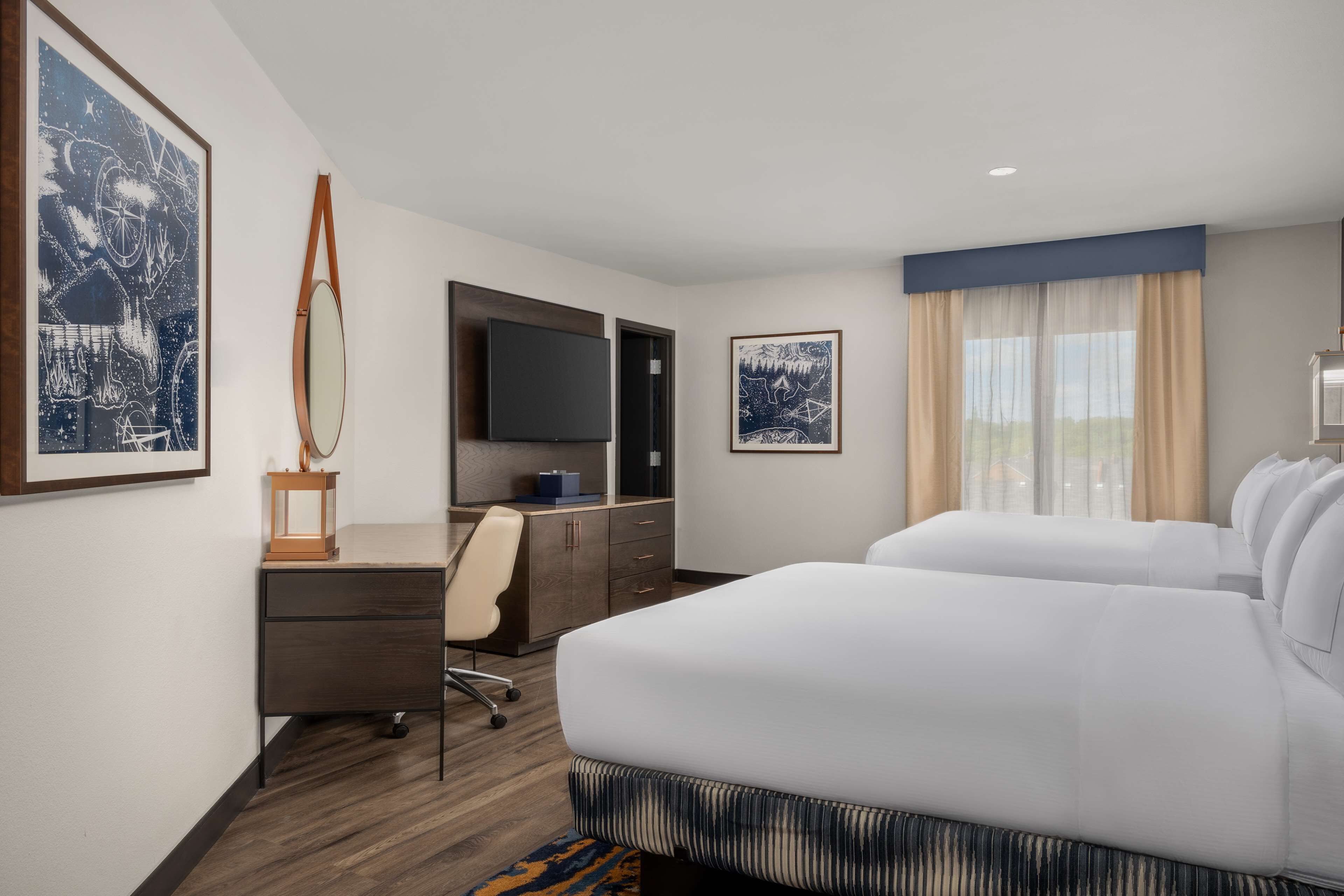 A hotel room with a large bed, a desk with a chair, a flat-screen TV, and artwork on the walls.