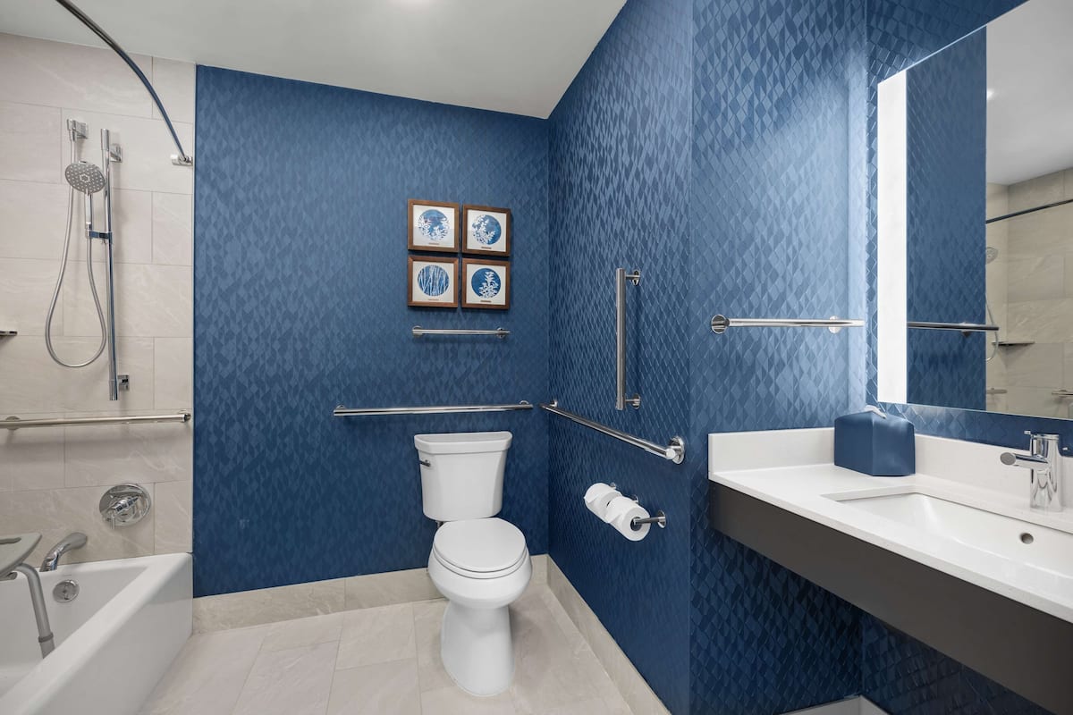 Un baño moderno con una pared azul, un inodoro blanco, una bañera y un lavabo con espejo.