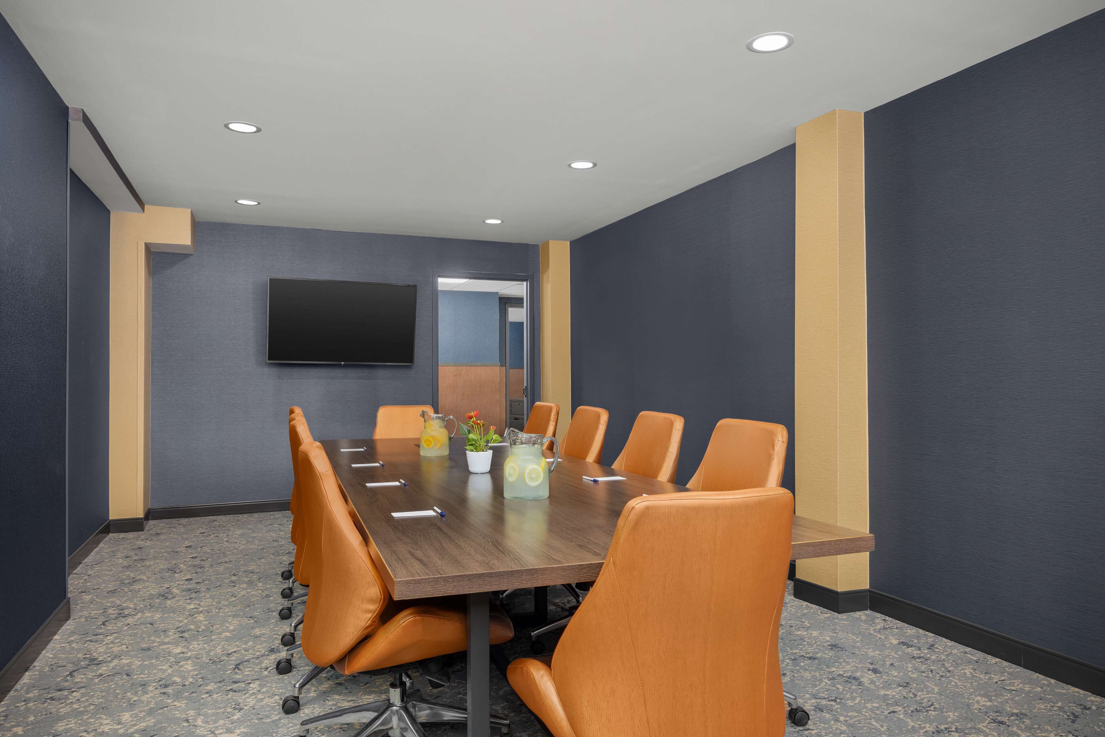 A conference room with a long table, orange chairs, a flat-screen TV, and a small plant on the table.