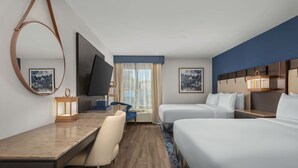 A hotel room with a desk, two beds, a TV, and artwork on the walls.