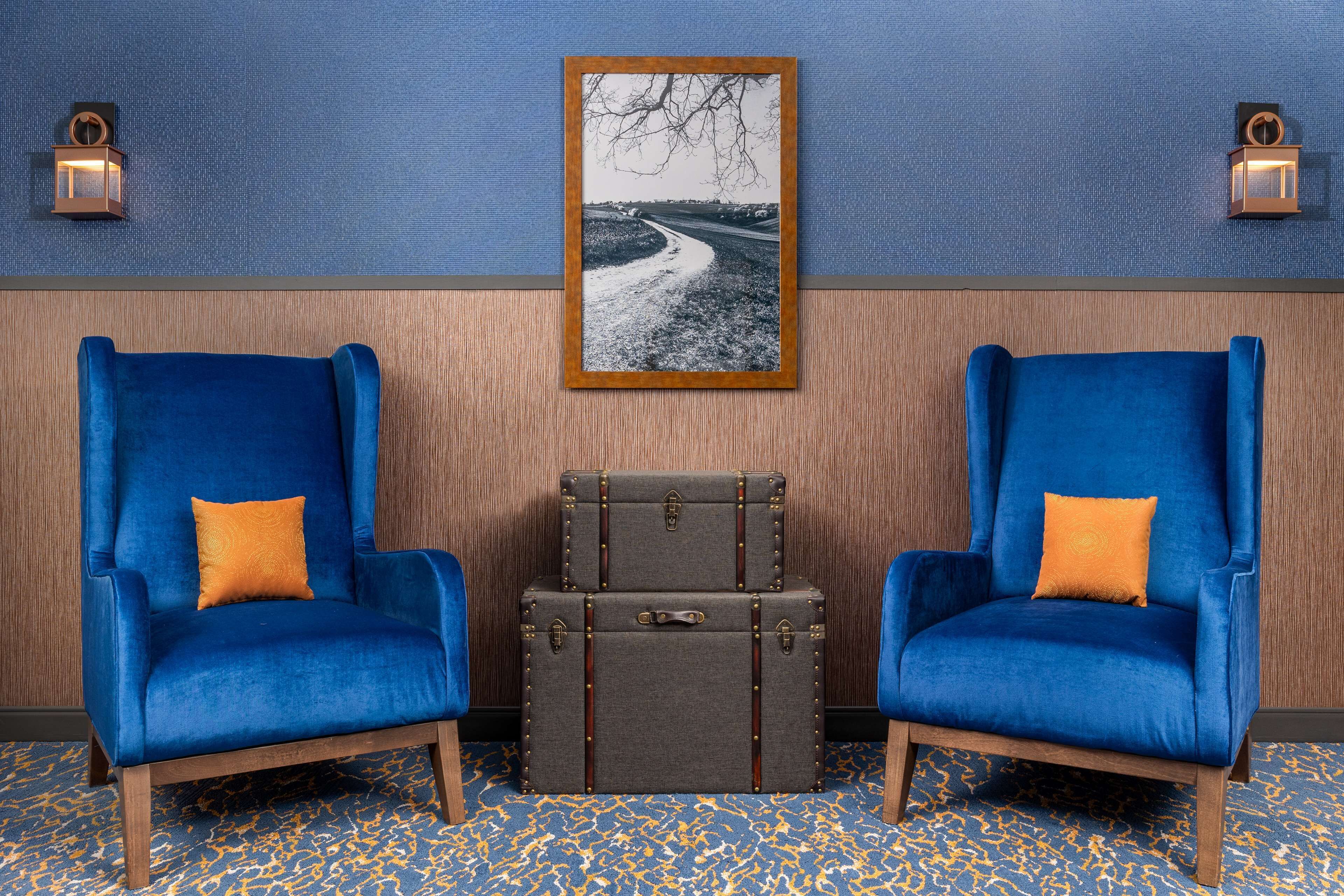 Dos sillones azules con cojines naranjas, un suelo de madera con diseño azul y amarillo, y una fotografía en blanco y negro enmarcada en la pared.