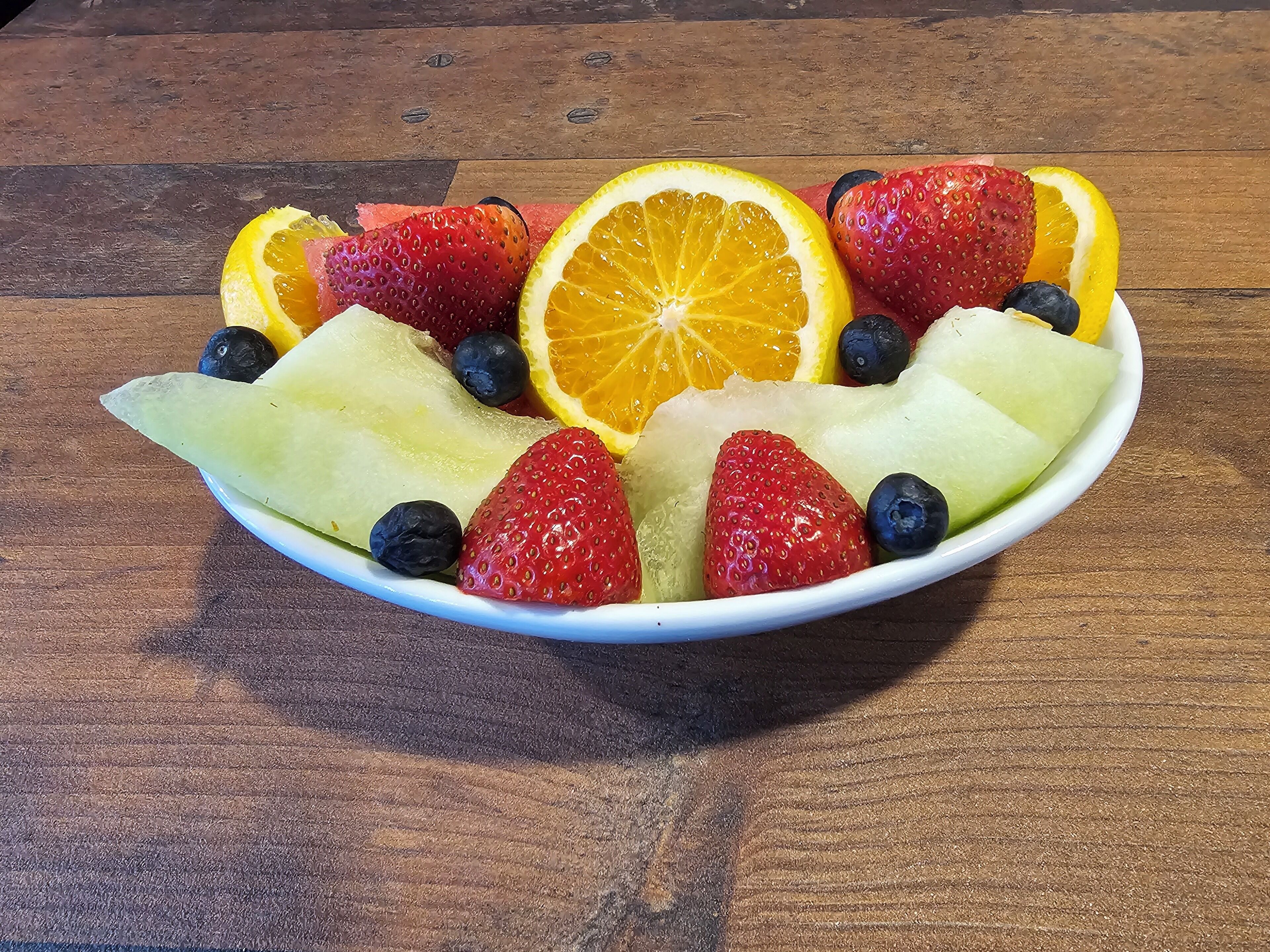 A bowl of sliced fruits including strawberries, blueberries, and orange slices on a wooden table.