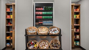 A vending machine with various beverages and snacks, surrounded by shelves stocked with packaged goods.