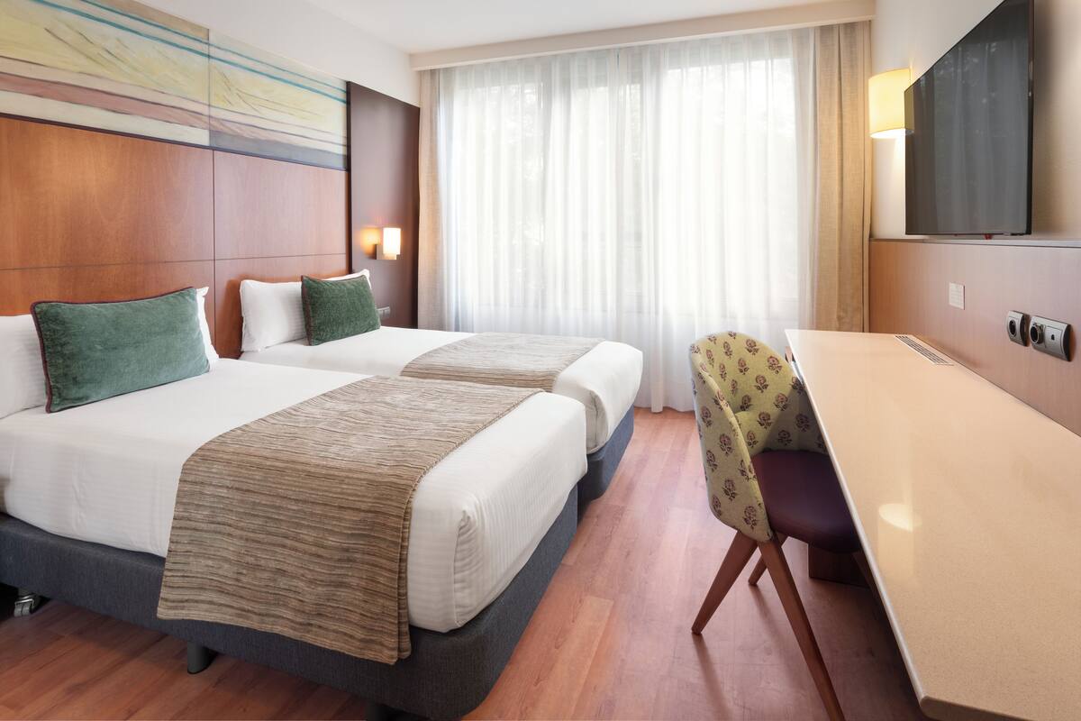 Habitación de hotel con dos camas, un escritorio, una silla, un televisor y una ventana con cortinas.