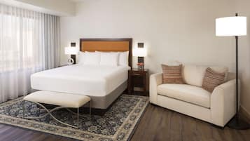 A hotel room with a large bed, a bedside table with a lamp, a sofa, and a floor lamp.