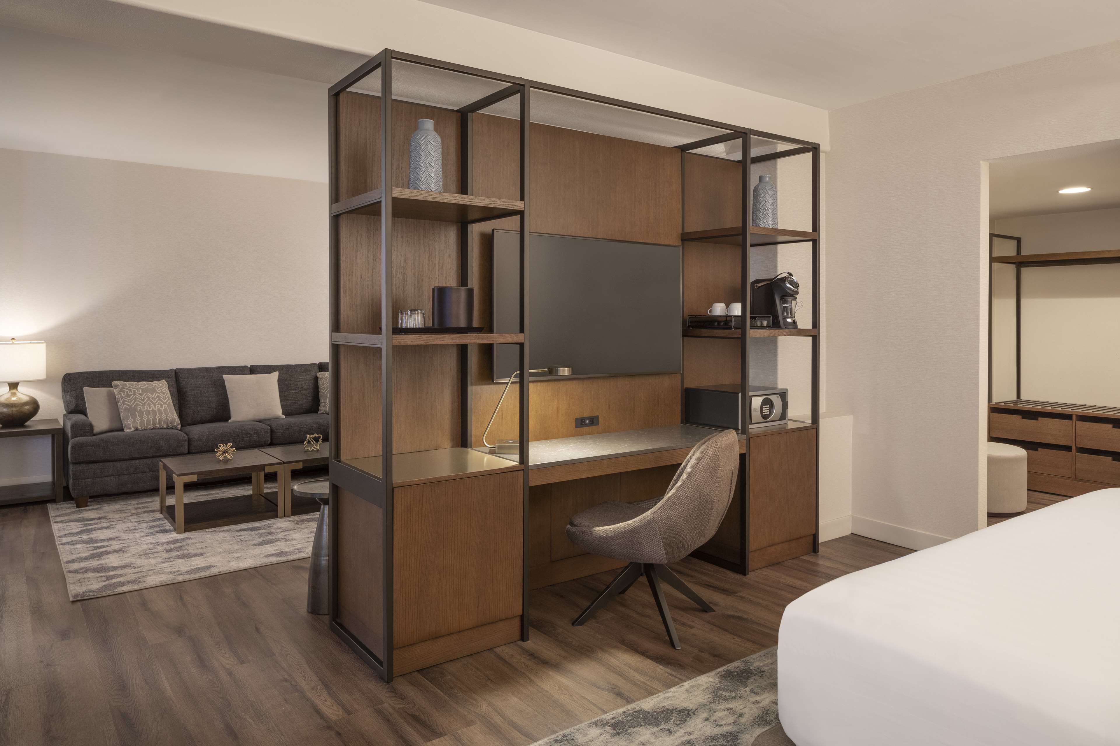 A modern hotel room with a wooden desk, a comfortable sofa, a flat-screen TV, and a bed.