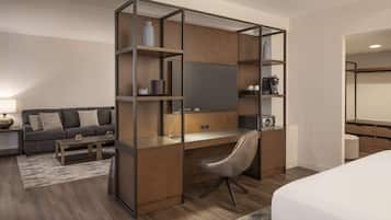 A modern hotel room with a wooden desk, a comfortable sofa, a flat-screen TV, and a bed.