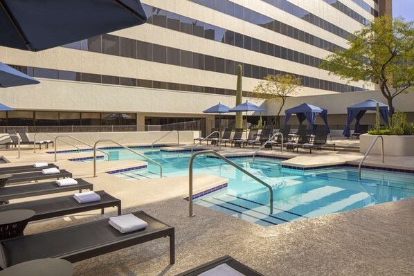 A pool area with lounge chairs, umbrellas, and a cactus.