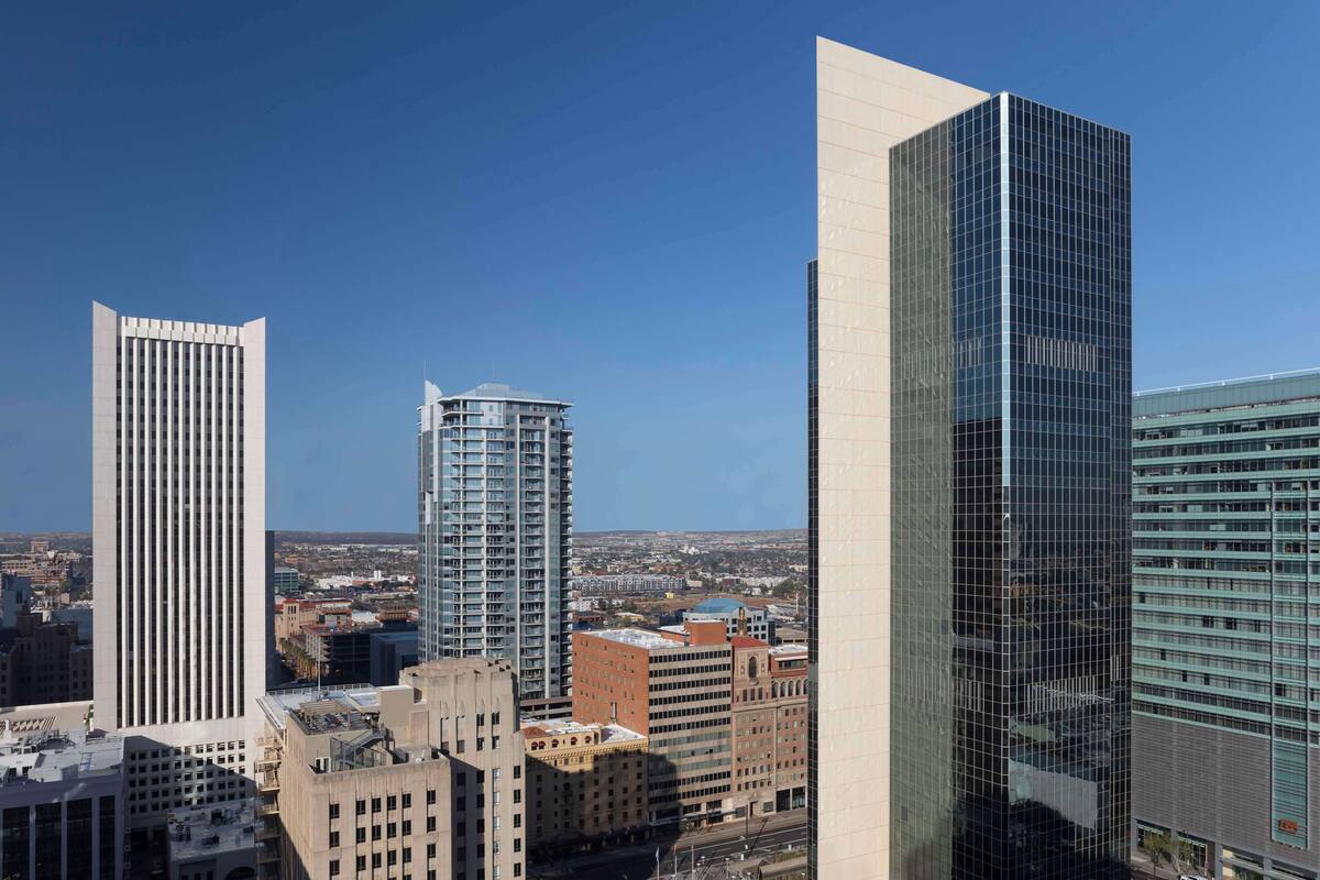 A cityscape with modern high-rise buildings, including a prominent glass skyscraper and a cylindrical tower.