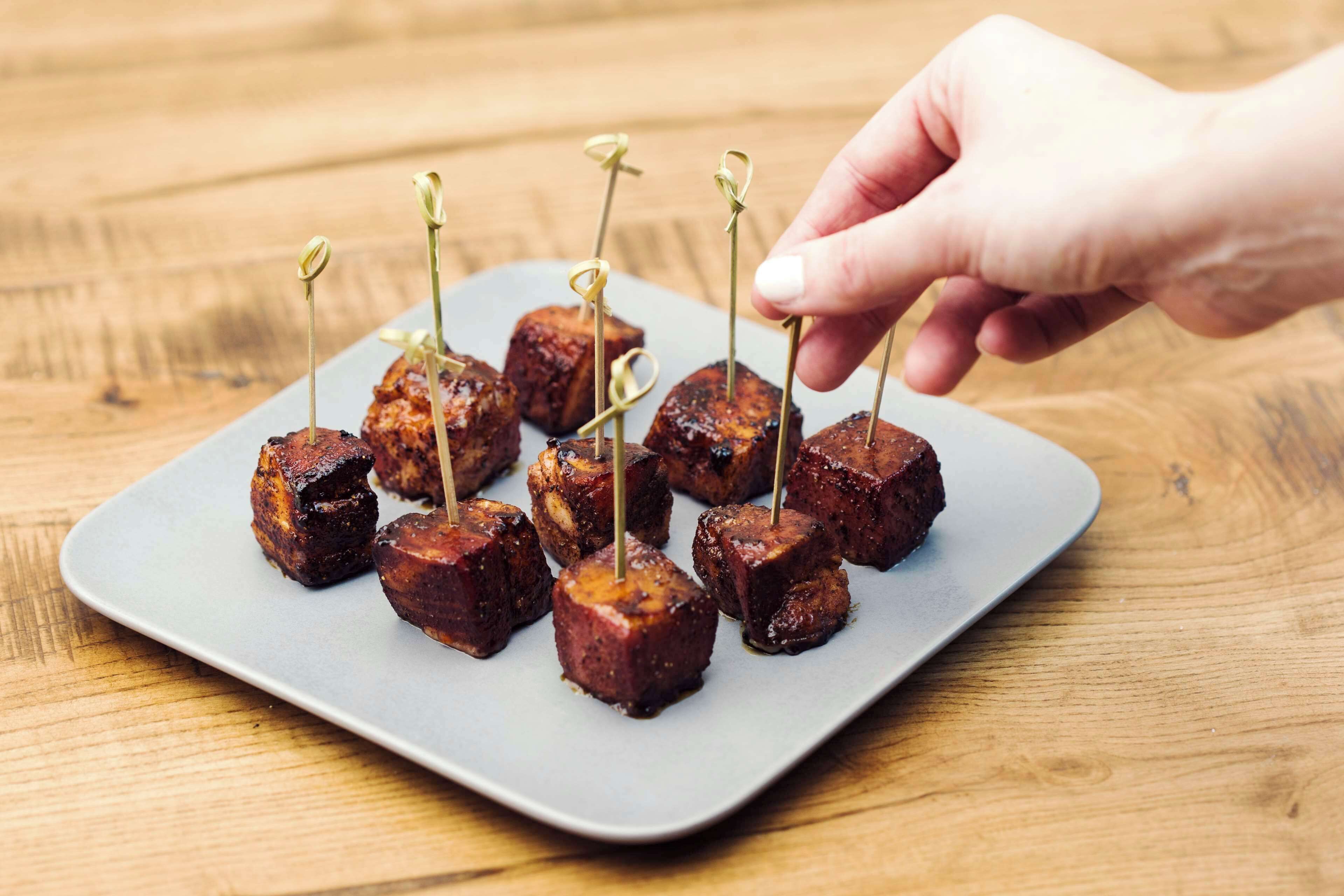 Une main dépose un cure-dent sur une brochette de viande, qui se trouve sur une assiette.