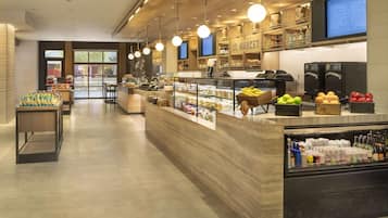 A modern cafe interior with a central counter, display cases with food items, and a digital menu board.